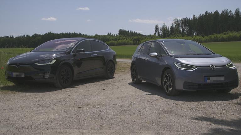"planet e.: Mythos Elektroauto - Revolution oder Reinfall?": Ein Tesla Model X und ein VW ID.3 stehen nebeneinander auf einem Parkplatz, im Hintergrund sieht man Wiese und Wald.