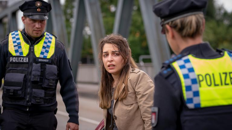 "Notruf Hafenkante - Kleine Hafenrundfahrt": Der Polizist Nick Brandt (Raúl Richter) und seine Kollegin Franzi Jung (Rhea Harder-Vennewald) stehen am Straßenrand. Zwischen ihnen, an ihren Pkw gelehnt,  steht Faiza Melek (Nisan Arikan). Sie blickt verstört zu Franzi.