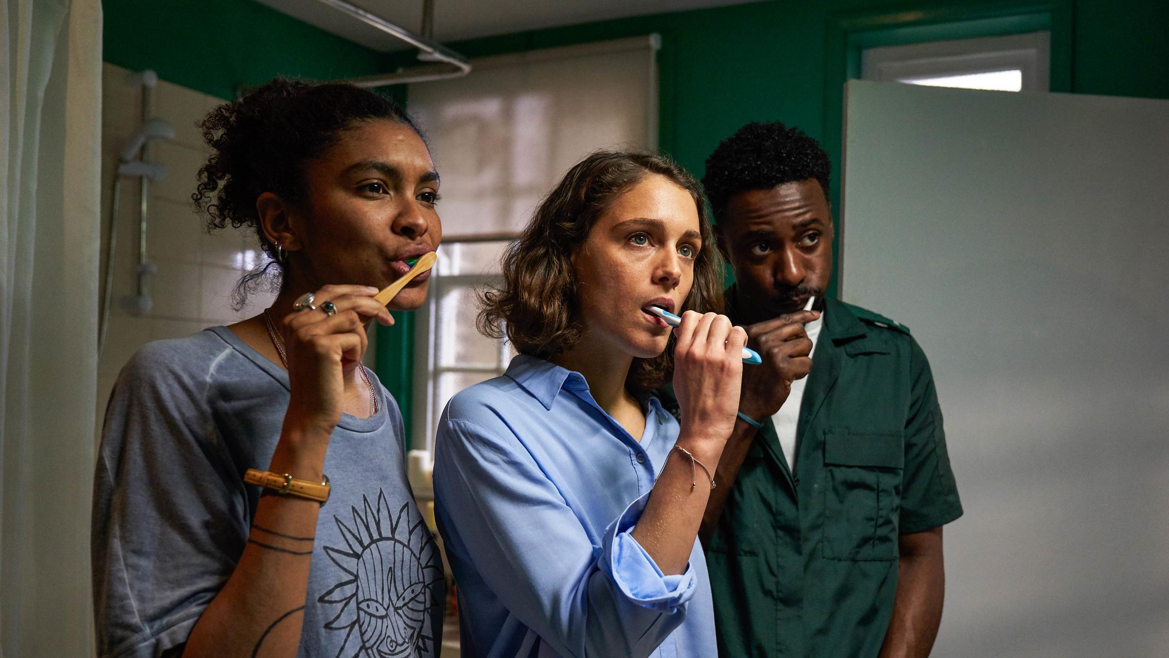 "Trigonometry - Stille Sehnsucht": Gemma (Thalissa Teixeira), Ray (Ariane Labed) und Kieran (Gary Carr) stehen nebeneinander im Badezimmer und putzen sich die Zähne. Gemma lächelt, während Ray und Kieran ernst dreinblicken.
