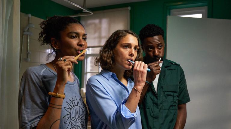 "Trigonometry - Stille Sehnsucht": Gemma (Thalissa Teixeira), Ray (Ariane Labed) und Kieran (Gary Carr) stehen nebeneinander im Badezimmer und putzen sich die Zähne. Gemma lächelt, während Ray und Kieran ernst dreinblicken.
