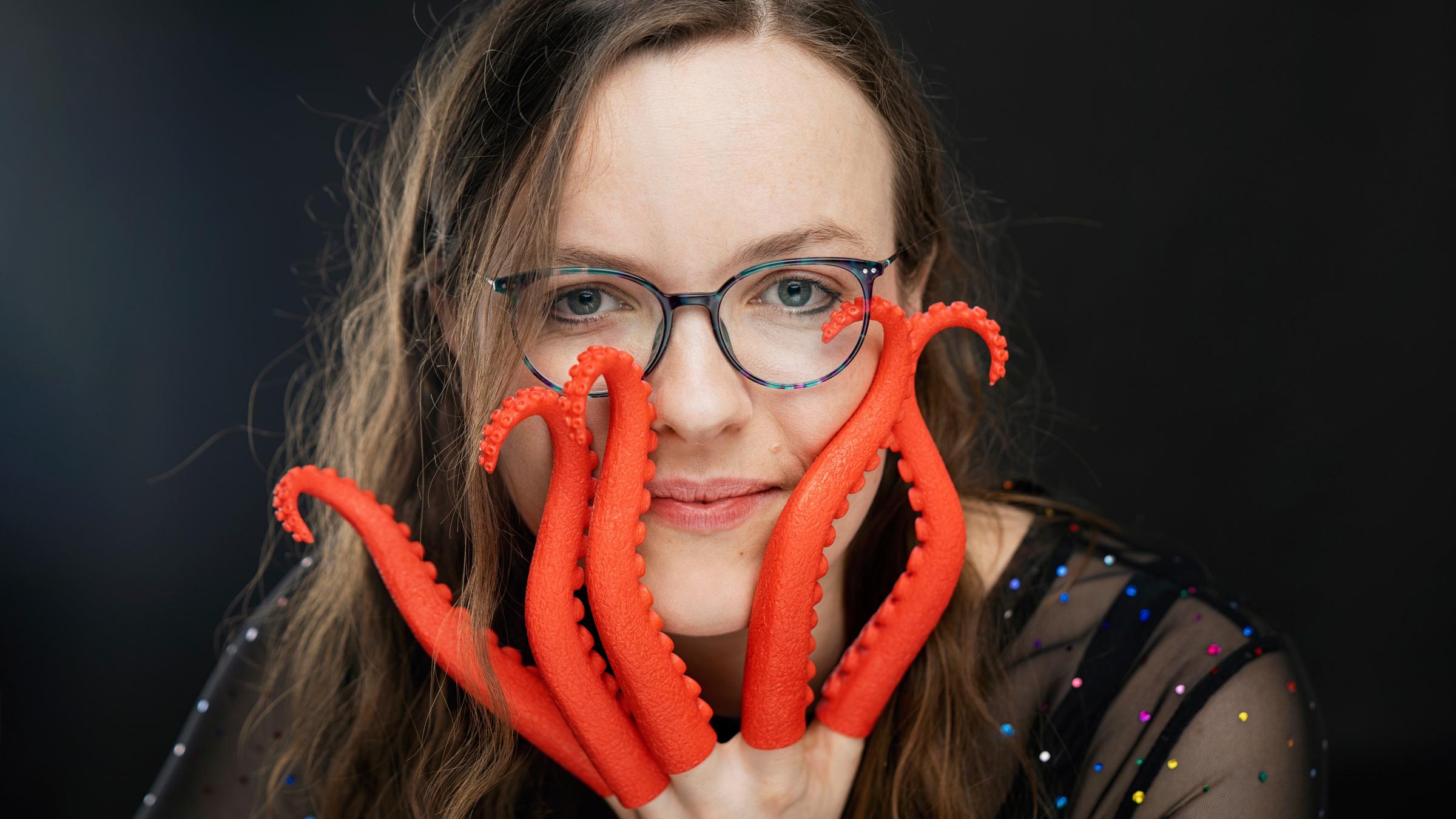 "Helene Bockhorst: Die Bekenntnisse der Hochstaplerin Helene Bockhorst": Porträt von Helene Bockhorst. Sie schaut in die Kamera und hält ihre linke Hand teilweise vor ihr Gesicht. An ihren Fingern befinden sich rote Plastik-Tintenfischarme.