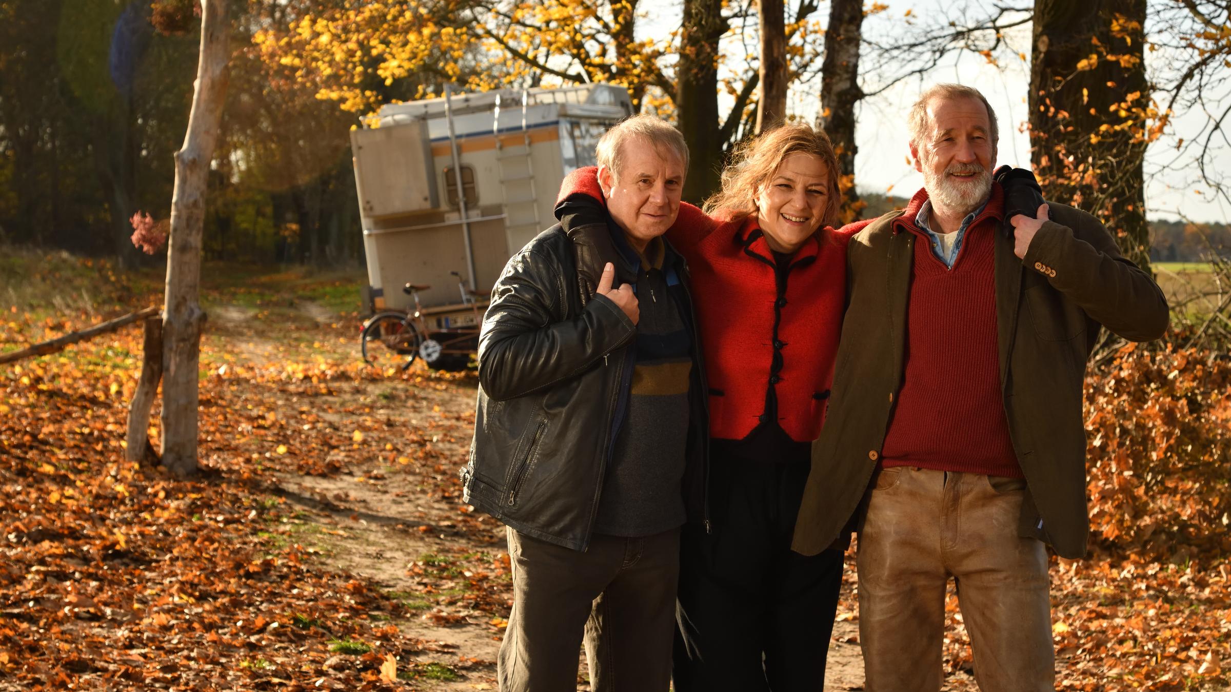 "Endlich Witwer - Forever Young": Auf dem Weg zum Wohnmobil steht Petra Schultheiss (Martina Gedeck) zwischen Georg Weiser (Joachim Król), ) und Jürgen König (Peter Lohmeyer) und stützt sich mit den Armen auf deren Schultern ab.