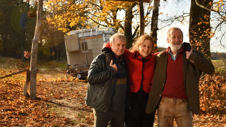 "Endlich Witwer - Forever Young": Auf dem Weg zum Wohnmobil steht Petra Schultheiss (Martina Gedeck) zwischen Georg Weiser (Joachim Król), ) und Jürgen König (Peter Lohmeyer) und stützt sich mit den Armen auf deren Schultern ab.