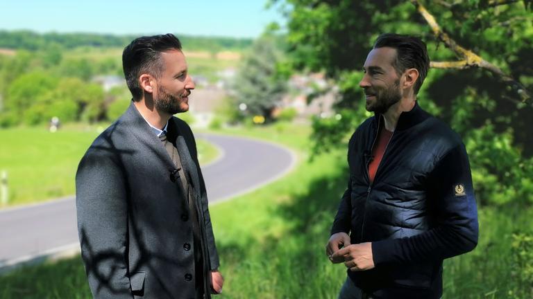 "XY gelöst": Staatsanwalt Thomas Hauburger und Sven Voss stehen tagsüber gemeinsam am Straßenrand einer Landstraße und unterhalten sich. Im Hintergrund ist ein Ortschaft.