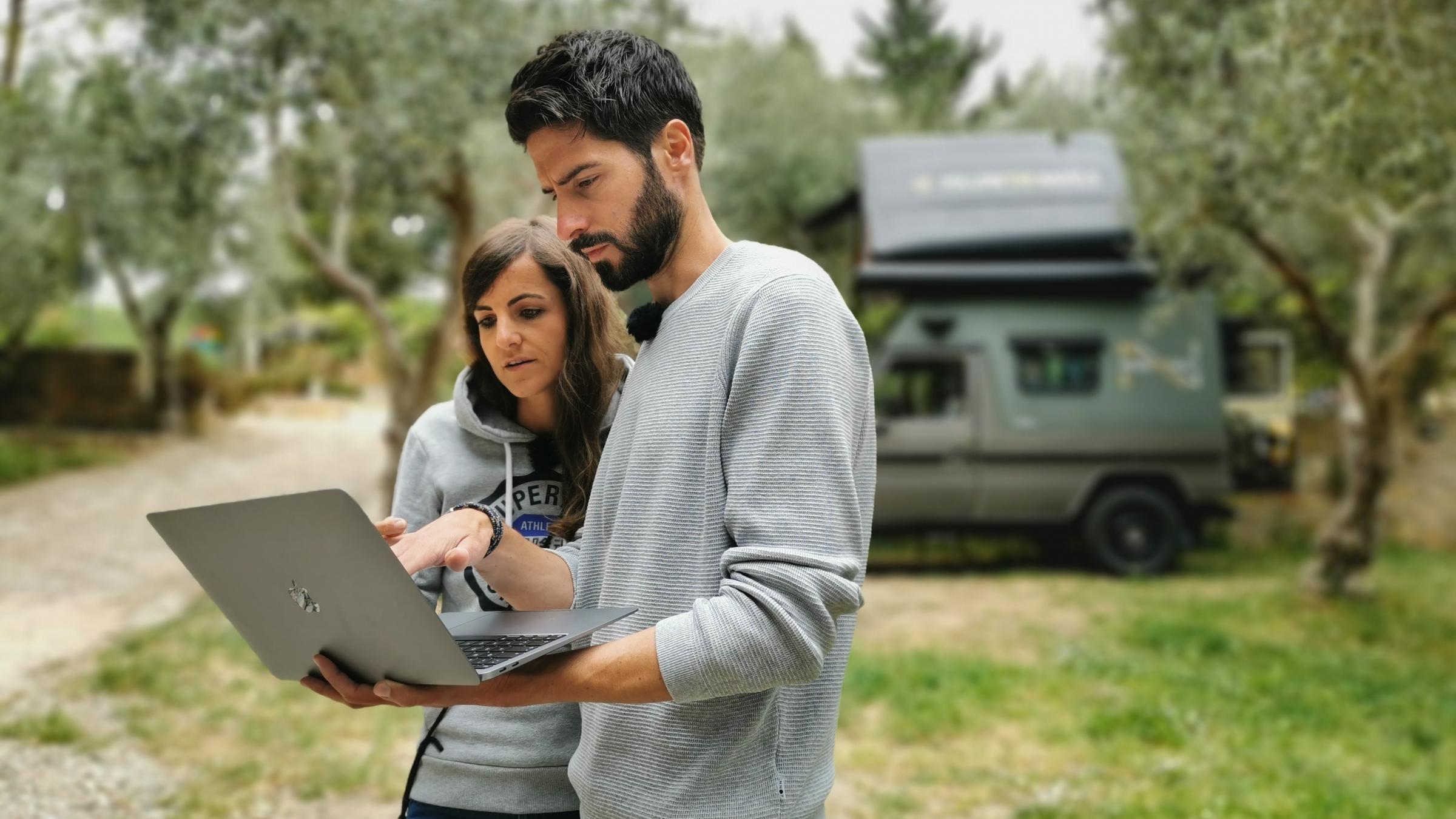 "WISO-Dokumentation: New Work. Die Zukunft der Arbeit": Jan Navel, ein großer dunkelhaariger Mann mit Bart und Greta Navel, eine Frau mit langen dunklen Haaren, stehen mit einem Notebook in der Hand  inmitten der Natur und schauen unzufrieden auf den Bildschirm. Im Hintergrund erkennt man unscharf den Camper-Van des Ehepaars.