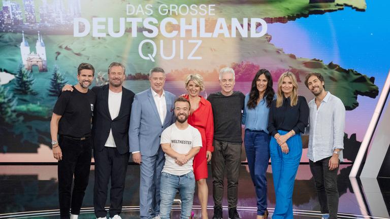"Das große Deutschland-Quiz": Tom Beck, Sasha, Joachim Llambi, Mathias Mester, Sabine Heinrich, Michael Mittermeier, Bettina Zimmermann, Kim Fisher und Max Giesinger stehen vor dem Sendungslogo. Alle lächeln in die Kamera.