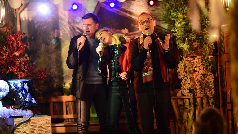 "München Mord – Schwarze Rosen": Harald Neuhauser (Marcus Mittermeier), Angelika Flierl (Bernadette Heerwagen) und Ludwig Schaller (Alexander Held) stehen jeweils mit einem Mikrofon in der Hand, zu dritt Arm in Arm, auf einer kleinen Bühne und singen.