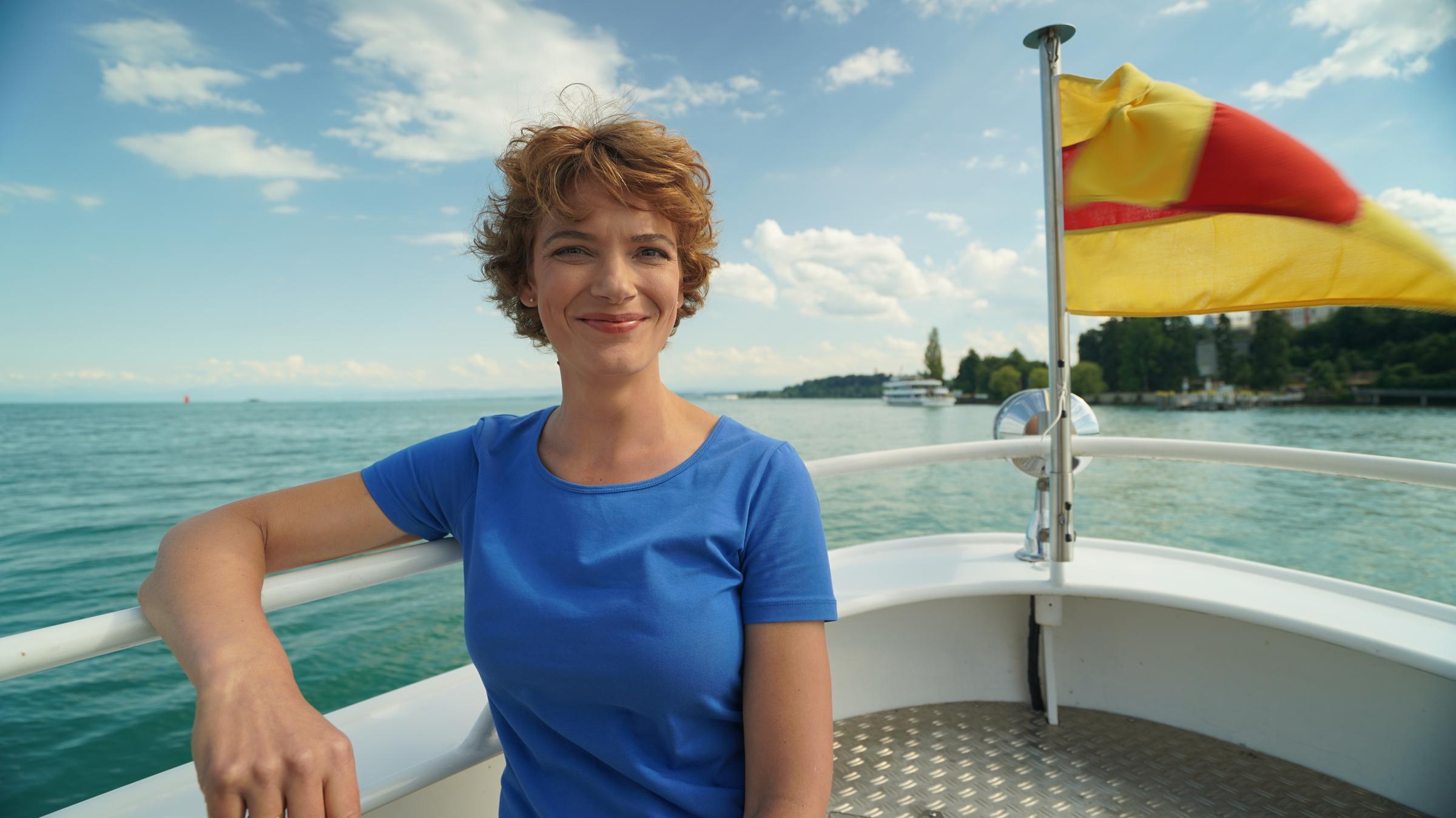 Terra Xpress: Faszination Bodensee - Leben am Wasser": Moderatorin Lena Ganschow sitzt in der Spitze eines Bootes: Im Hintergrund weht eine gelb-rote Fahne und man sieht in der Ferne Land.