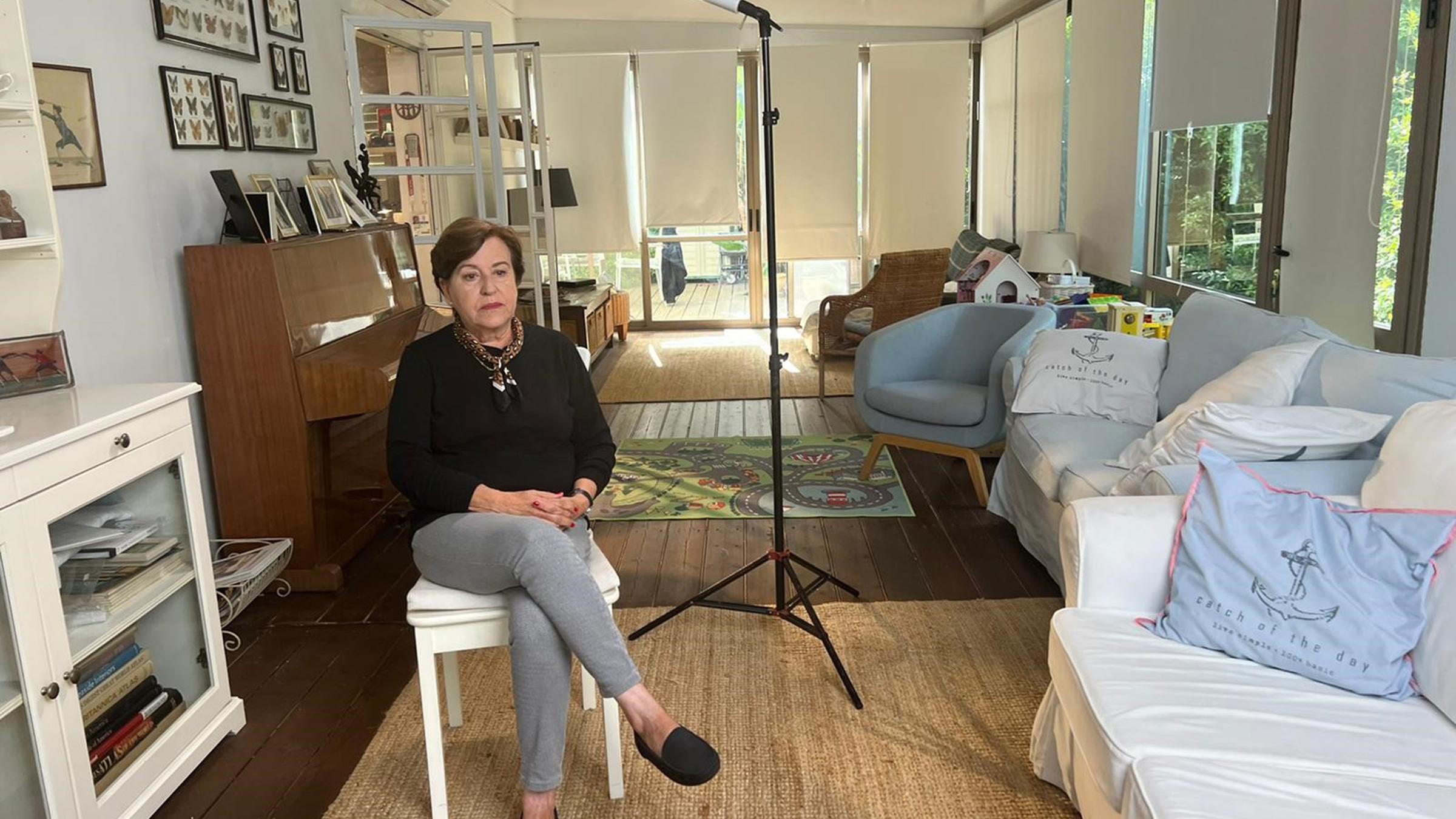 "München '72 - Anschlag auf Olympia. Heitere Spiele, tödlicher Terror": Ankie Spitzer, deren Ehemann André von Terroristen beim Olympia-Attentat getötet wurde, wird gerade für ein Interview vorbereitet. Sie sitzt auf einem Stuhl im Wohnzimmer ihres Hauses. Neben ihr steht ein Scheinwerfer. Sie trägt einen schwarzen Pullover und eine graue Hose.