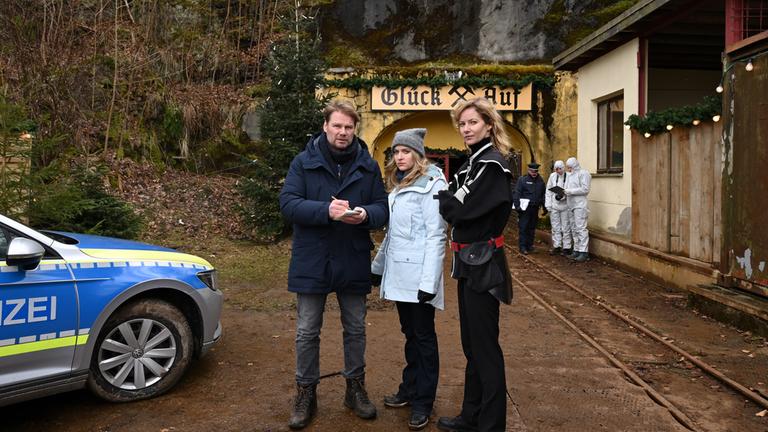 "Erzgebirgskrimi - Ein Mord zu Weihnachten": Robert Winkler (Kai Scheve), Karina Szabo (Lara Mandoki) und Saskia Bergelt (Teresa Weißbach) stehen vor einem Bergwerk. Es ist ein Polizeiauto zu sehen.