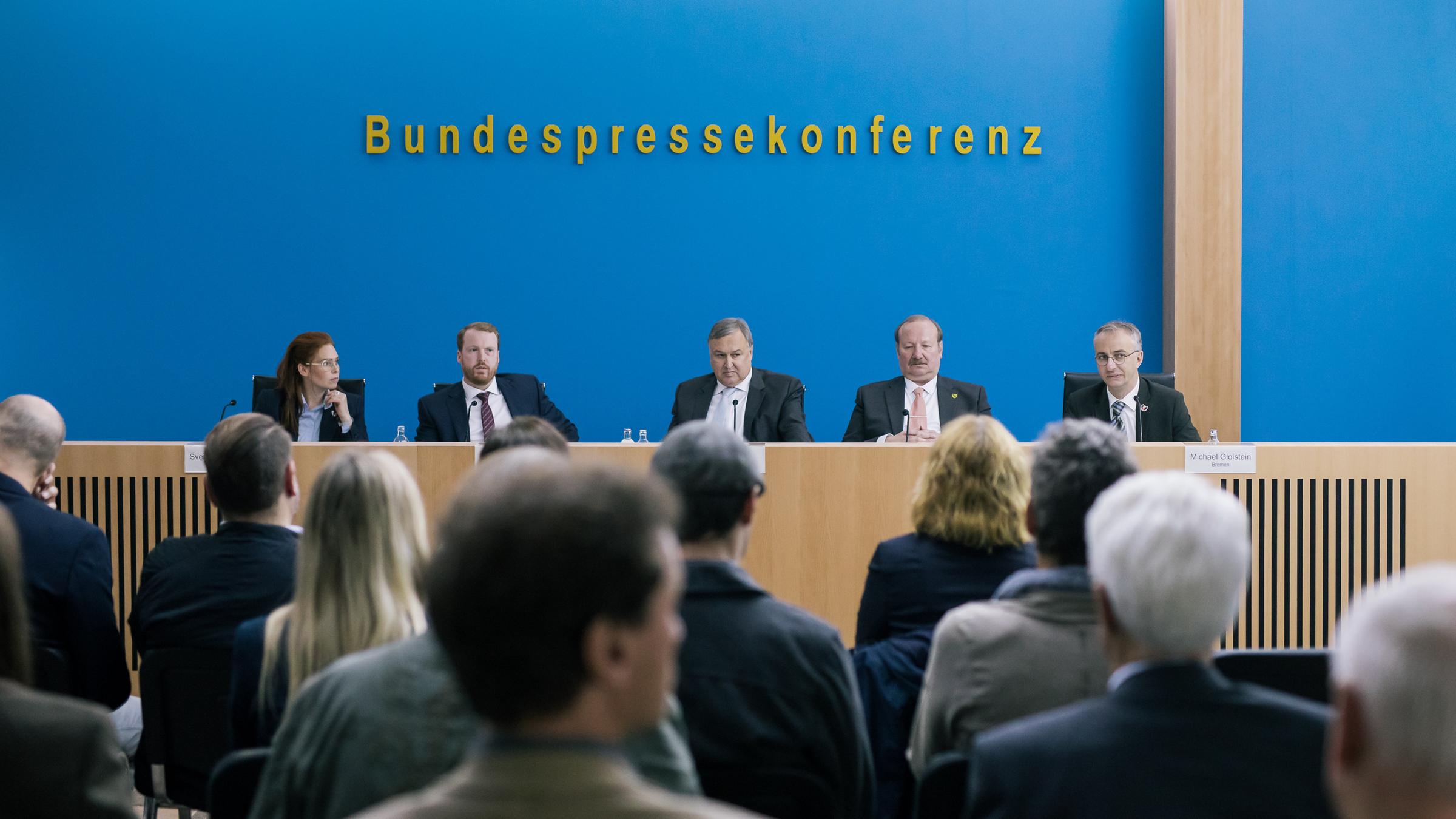 "ZDF Magazin Royal präsentiert: Die Innenministerkonferenz": Am langen Pult der Bundespressekonferenz sitzen fünf PolitikerInnen vor der typisch blauen BPK-Wand und stehen den Hauptstadtjournalisten Rede und Antwort. Schauspieler: Henny Reents, Ole Fischer, Christoph Zrenner und Jan Böhmermann.