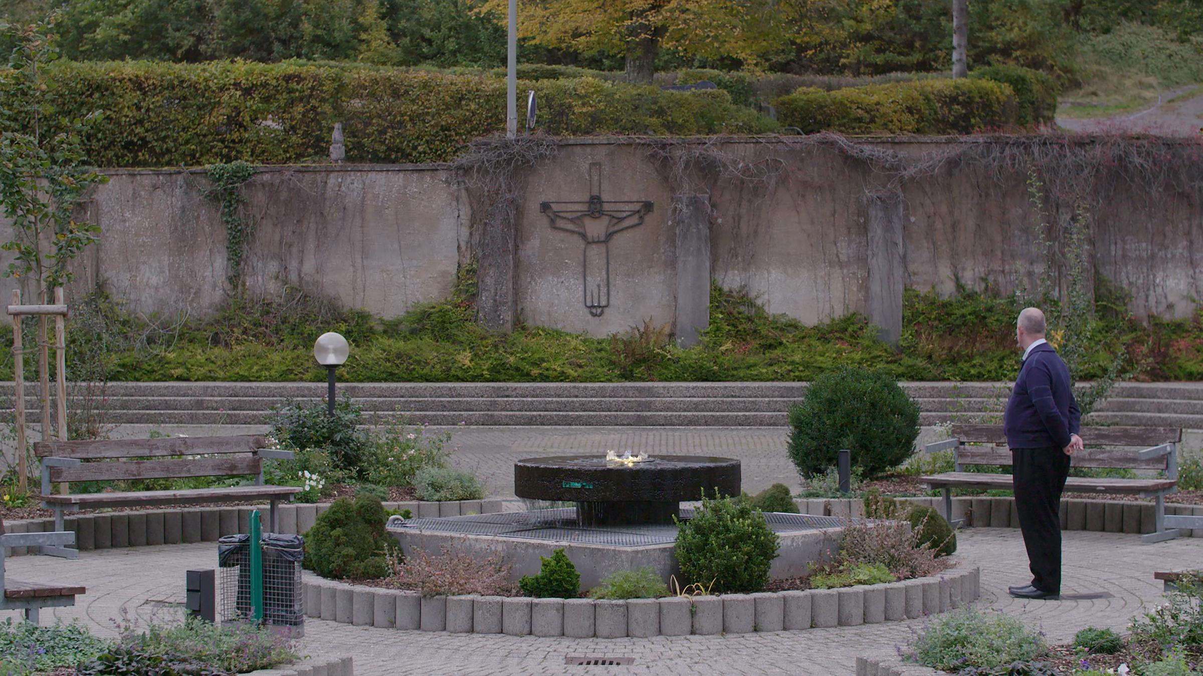 "37° Nicht vergessen, nie vergeben - Mein Leben nach dem Missbrauch": Klaus S. steht auf einem Platz mit einem großen Kreuz.