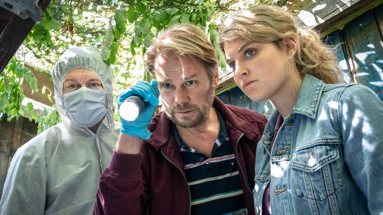 "Erzgebirgskrimi - Verhängnisvolle Recherche": Kriminaltechniker Maik (Adrian Topol), Hauptkommissar Robert Winkler (Kai Scheve) und Kommissarin Karina Szabo (Lara Mandoki) stehen vor einem geöffneten Kofferraum eines Autos und schauen hinein.