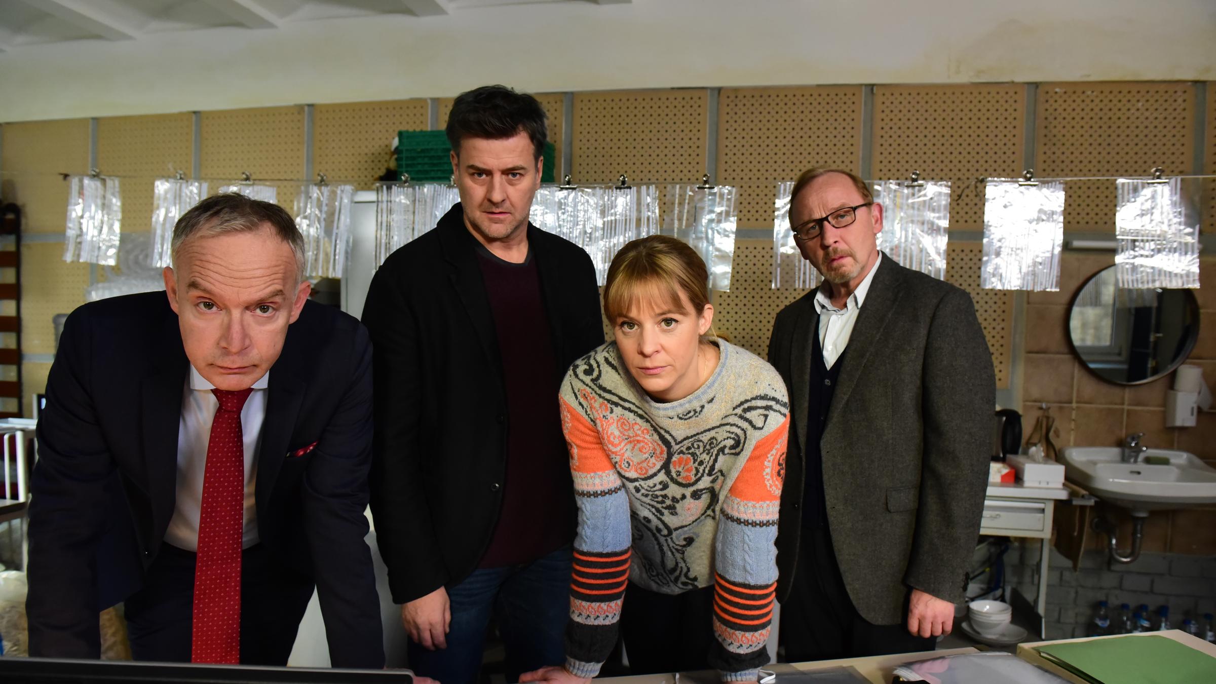 "München Mord - Dolce Vita": Helmut Zangel (Christoph Süß), Angelika Flierl (Bernadette Heerwagen), Harald Neuhauser (Marcus Mittermeier) und Ludwig Schaller (Alexander Held) schauen gemeinsam im Büro auf einen Computerbildschirm. Vor und hinter ihnen befinden sich zerschredderte Akten.