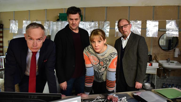 "München Mord - Dolce Vita": Helmut Zangel (Christoph Süß), Angelika Flierl (Bernadette Heerwagen), Harald Neuhauser (Marcus Mittermeier) und Ludwig Schaller (Alexander Held) schauen gemeinsam im Büro auf einen Computerbildschirm. Vor und hinter ihnen befinden sich zerschredderte Akten.