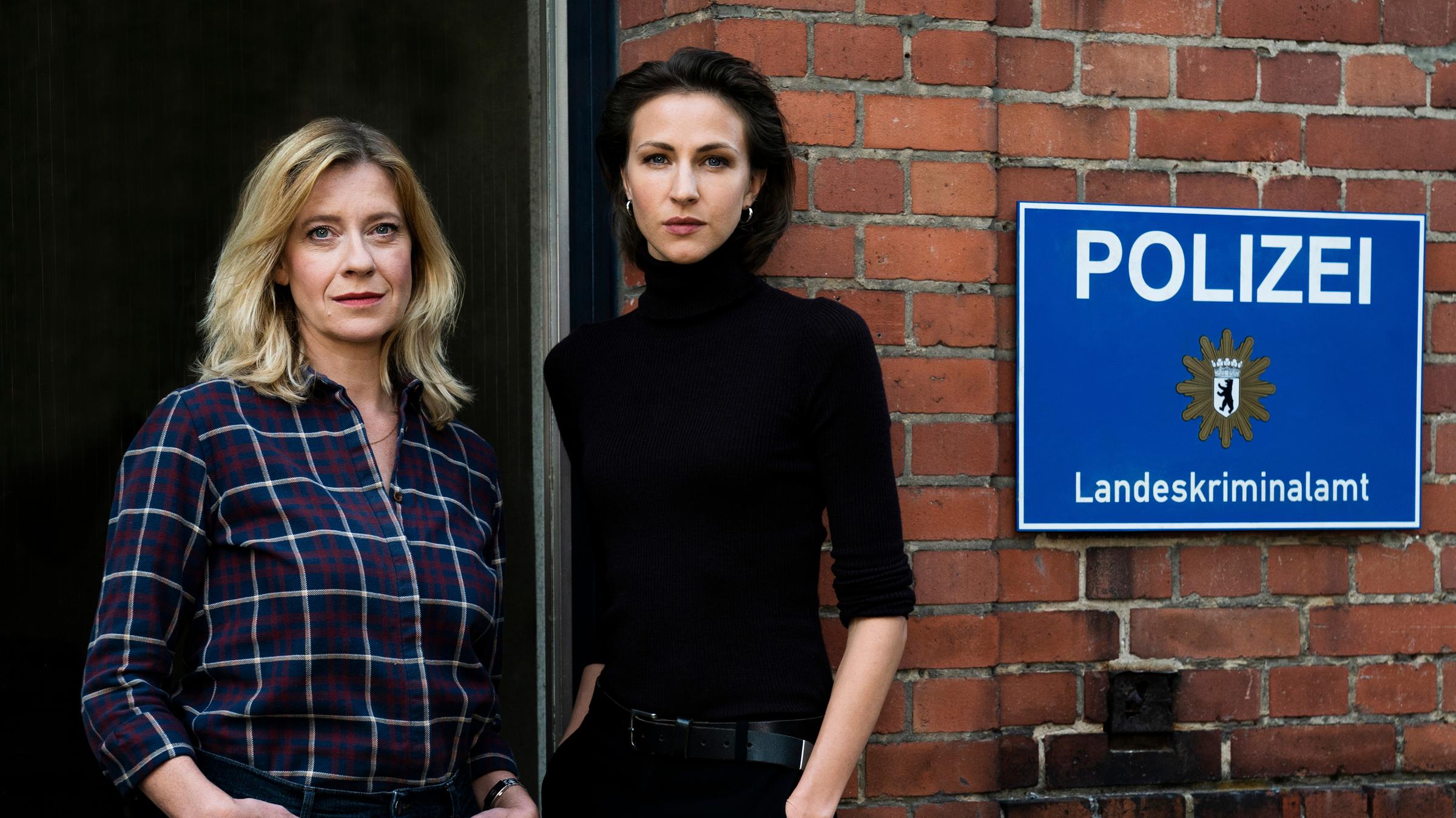 "Kolleginnen - Das böse Kind": Irene und Julia stehen zusammen vor einer Eingangstür. Neben ihnen ein Schild mit der Aufschrift Polizei.