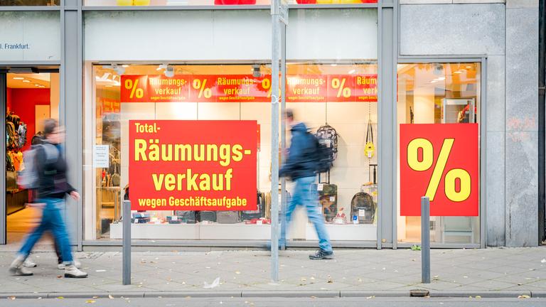 "ZDF.reportage: Wir schließen für immer - Einzelhändler in der Krise": Ladengeschäft mit beklebten Schaufenstern: "Total Räumungsverkauf wegen Geschäftsaufgabe". In der Unschärfe gehen Personen an dem Geschäft vorbei.