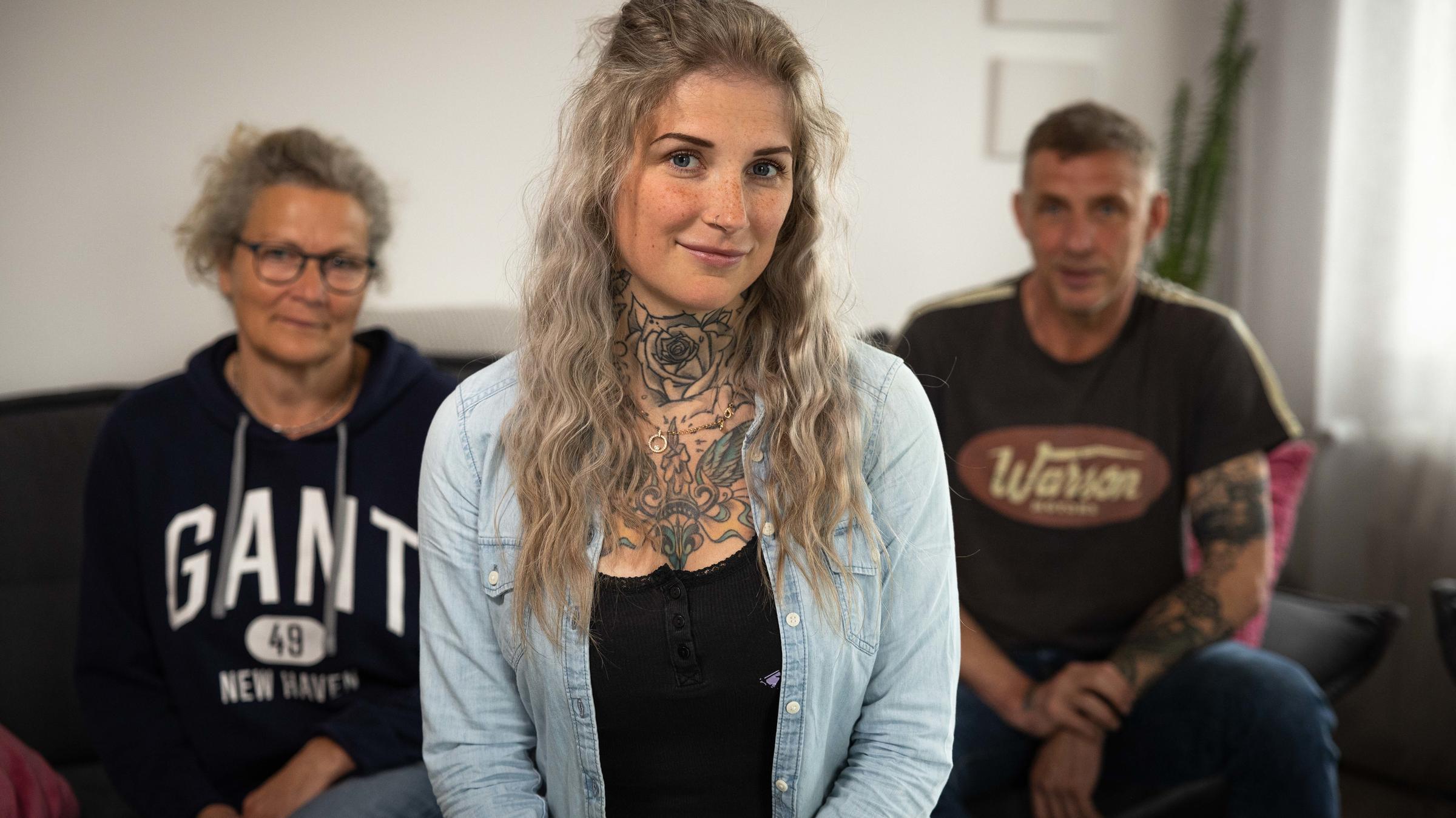   "37° Nesthocker - Wenn Kinder nicht ausziehen": Ve schaut lächelnd in die Kamera. Im Hintergrund sitzen eine Frau und ein Mann, es sind die Eltern der jungen Frau.