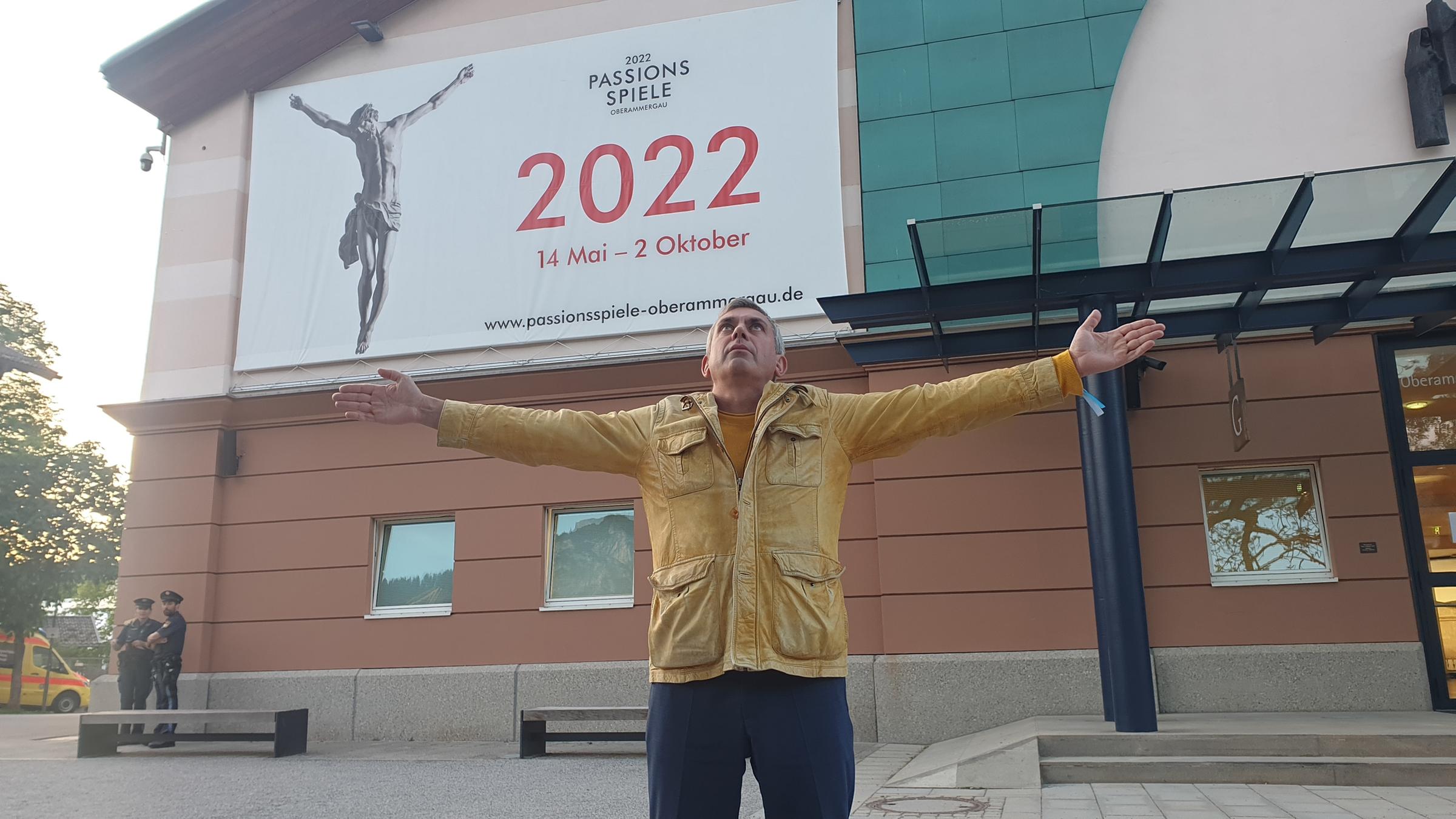 "Kaminer Inside: Passionsspiele Oberammergau": Wladimir Kaminer steht vor dem Eingang des Festspielhauses. Auf einem Banner über ihm sieht man Jesus am Kreuze. Kaminer breitet die Arme aus und ahmt das nach.
