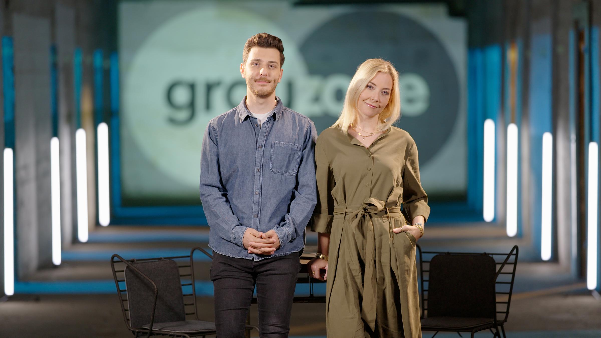 "ZDFzoom: Grauzone: Heavy Mental - Generation Depression?": Die Hosts Sissy Metzschke und Tarkan Bagci stehen nebeneinander in einem abgedunkelten Raum.