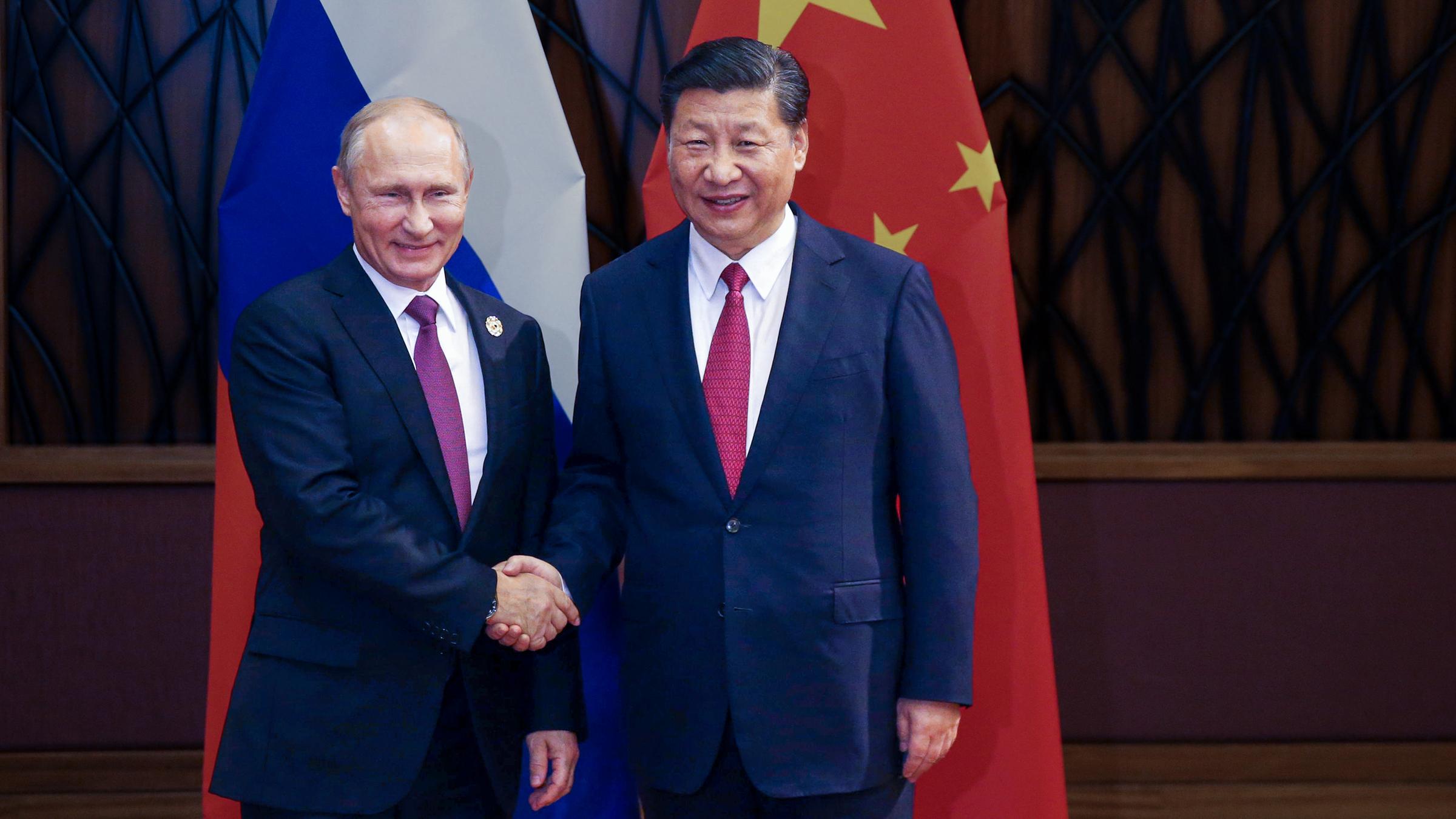 "ZDFzeit: Putin und Xi - Pakt gegen den Westen": Wladimir Putin und Xi Jinping stehen vor der russischen und der chinesischen Fahne und geben sich die Hand.