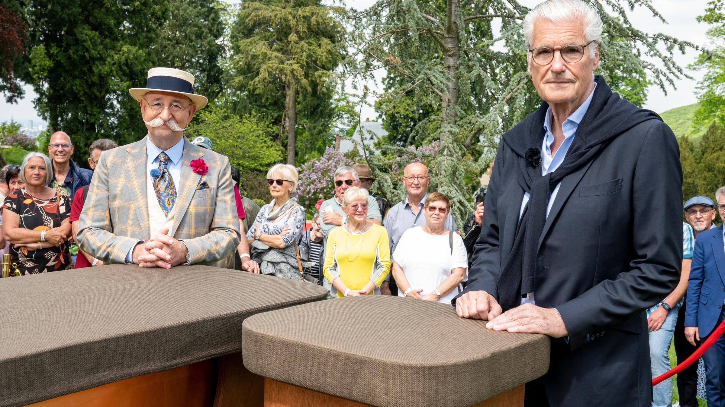 "Bares für Rares - Deutschlands größte Trödel-Show": Horst Lichter und Sky du Mont stehen hinter Tischen und lächeln in die Kamera. Im Hintergrund ist Publikum zu sehen.
