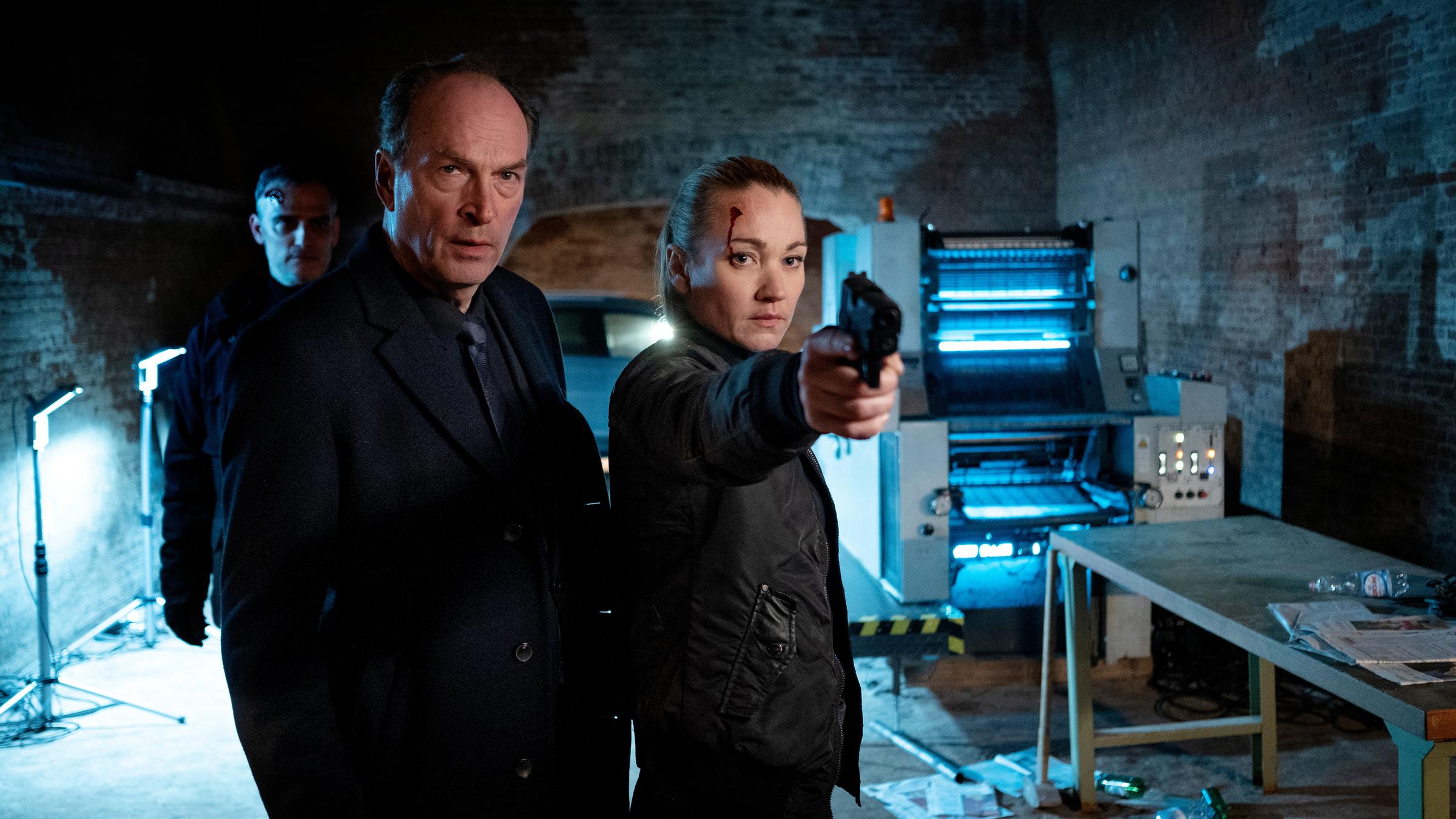 "Sarah Kohr - Geister der Vergangenheit": Anton Mehringer (Herbert Knaup) und Sarah Kohr (Lisa Maria Potthoff) stehen in einem schwach erleuchteten Kellerraum, in dem eine Druckmaschine steht. Sarah hat ihre Waffe gegzogen und zielt auf jemanden.