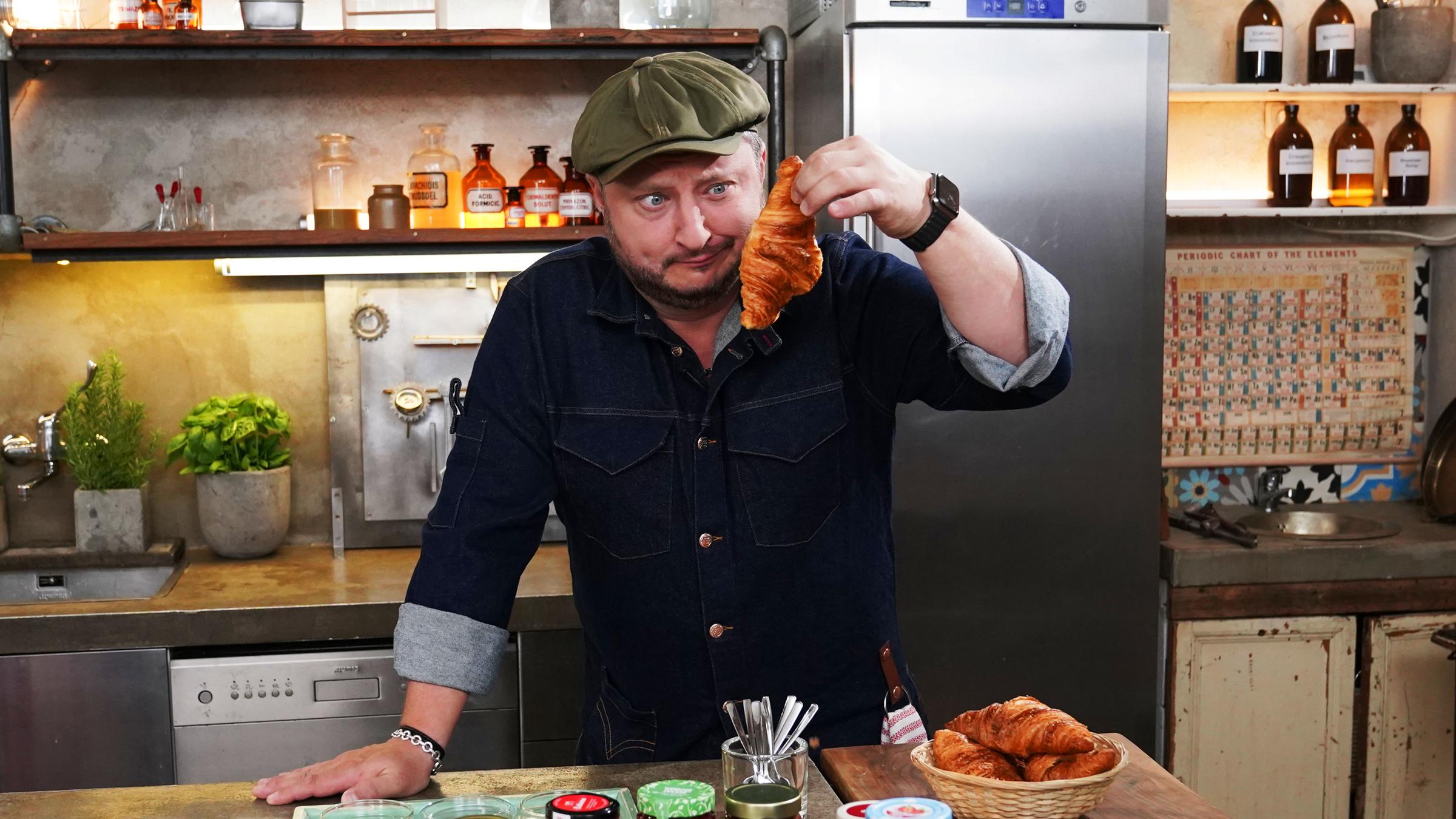 "Lebensmitteltricks - Lege packt aus: Fiese Frühstücks-Fallen": Sebastian Lege hat zuckerreduzierten Fruchtaufstrich eingekauft und wirft einen kritischen Blick auf ein Croissant.