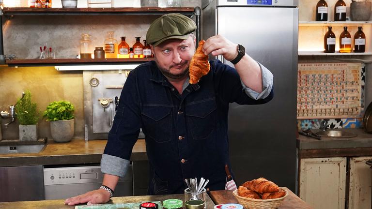 "Lebensmitteltricks - Lege packt aus: Fiese Frühstücks-Fallen": Sebastian Lege hat zuckerreduzierten Fruchtaufstrich eingekauft und wirft einen kritischen Blick auf ein Croissant.