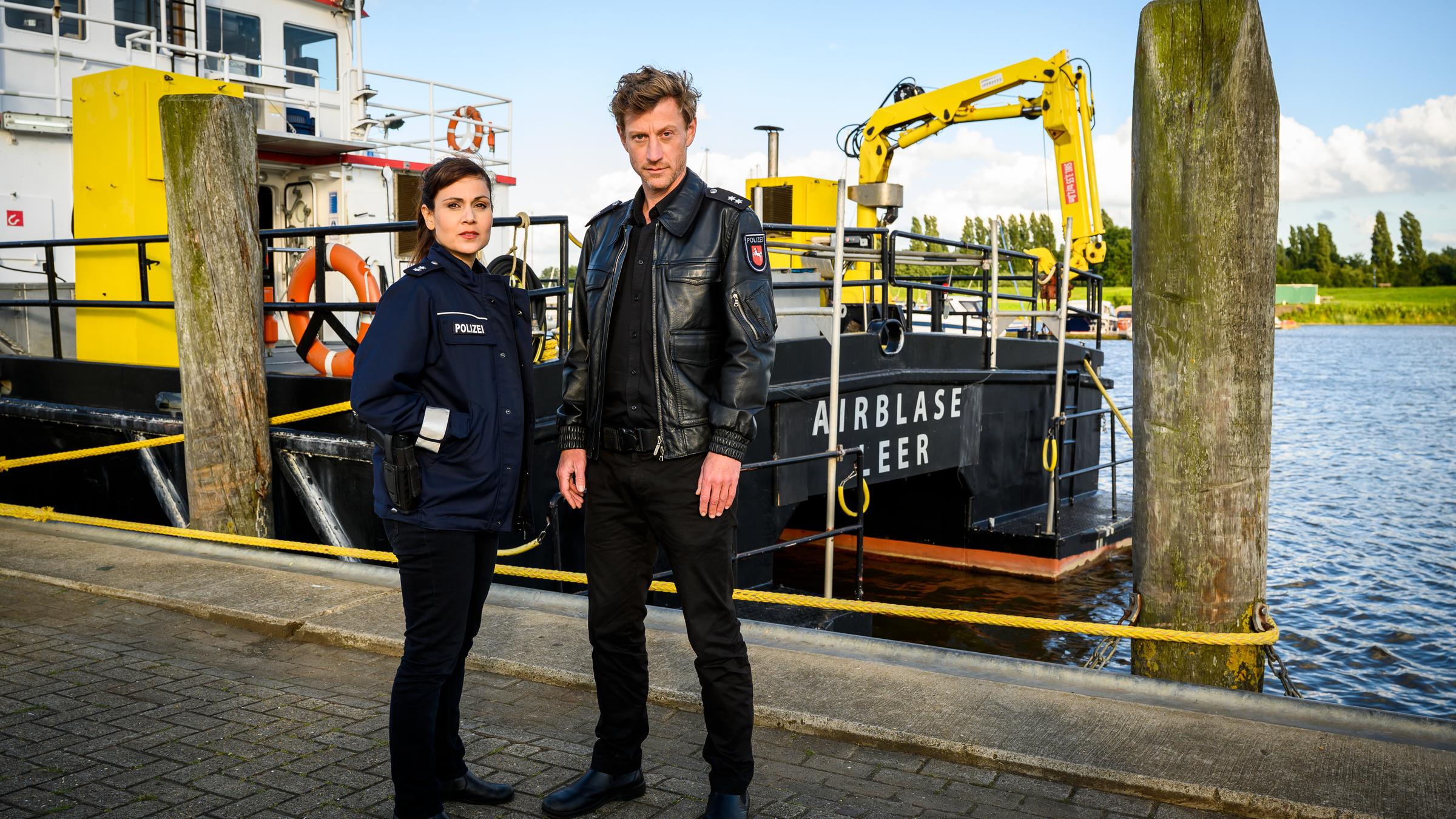 "Friesland - Prima Klima": Die beiden Polizisten Henk Cassens (Maxim Mehmet) und Süher Özlügül (Sophie Dal) stehen auf einem Bootssteg und schauen in die Kamera.