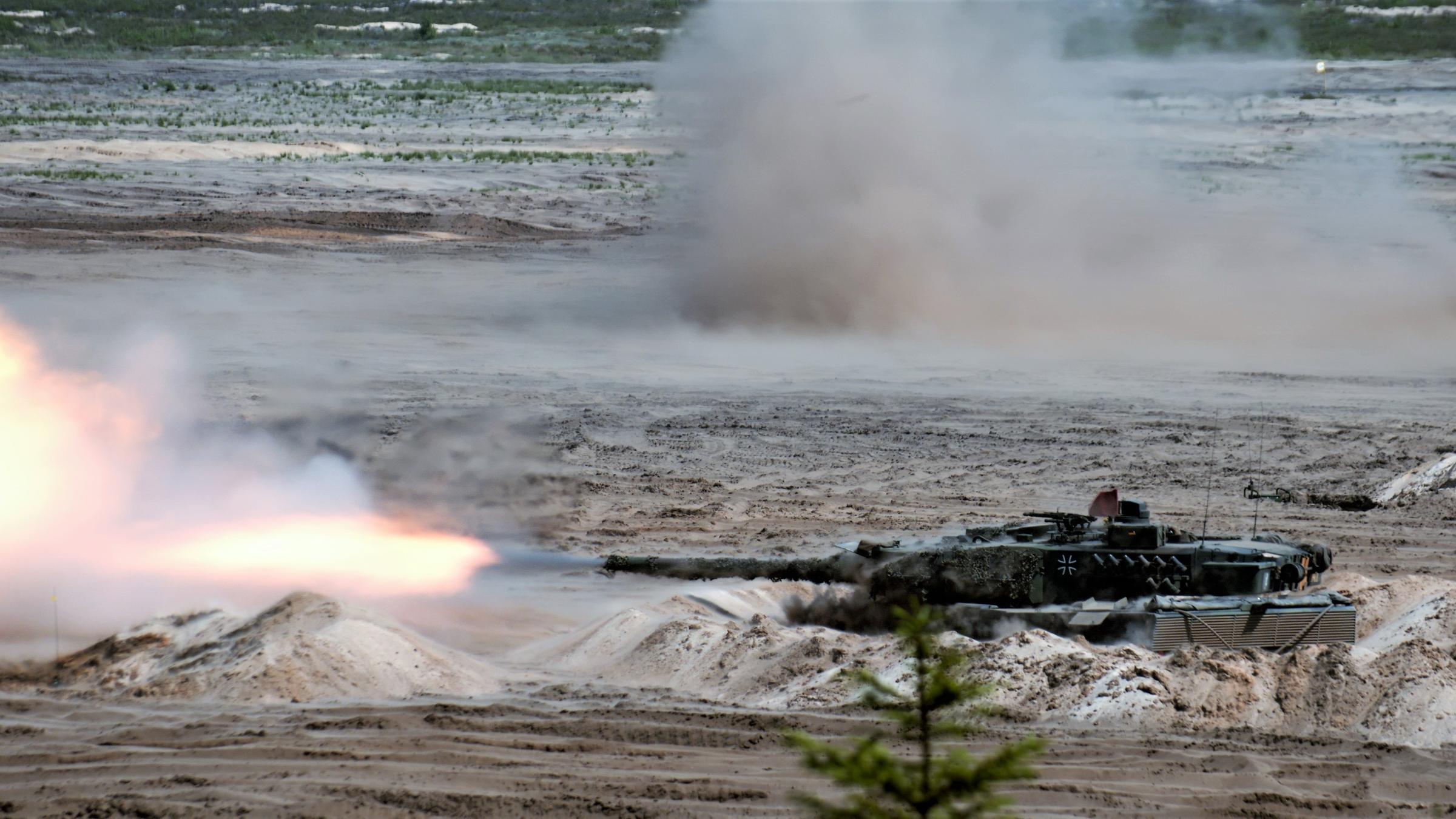 "ZDFzoom: Aufrüstung zur Abschreckung? - Europas neue Fronten": Ein Leopard-Kampfpanzer steht auf einem Übungsplatz und schießt eine Feuersalve ab. Im Hintergrund eine Explosion.