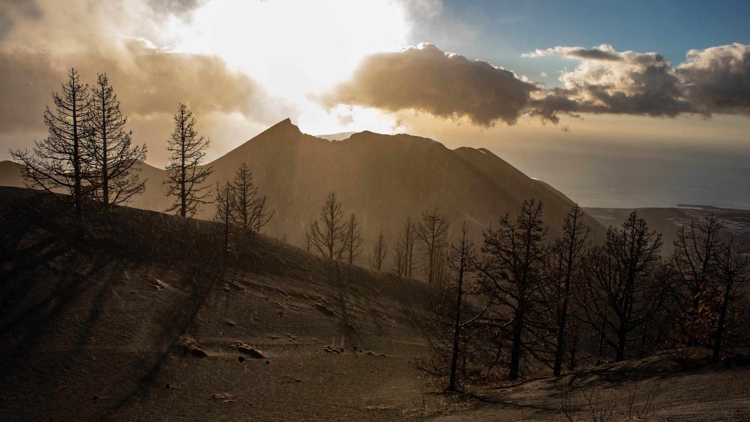 "La Palma - Leben mit dem Vulkan": Blick auf den Vulkan Cumre Vieja, der im Sonnenlicht liegt. Im Vordergrund aschebedecke Felder.