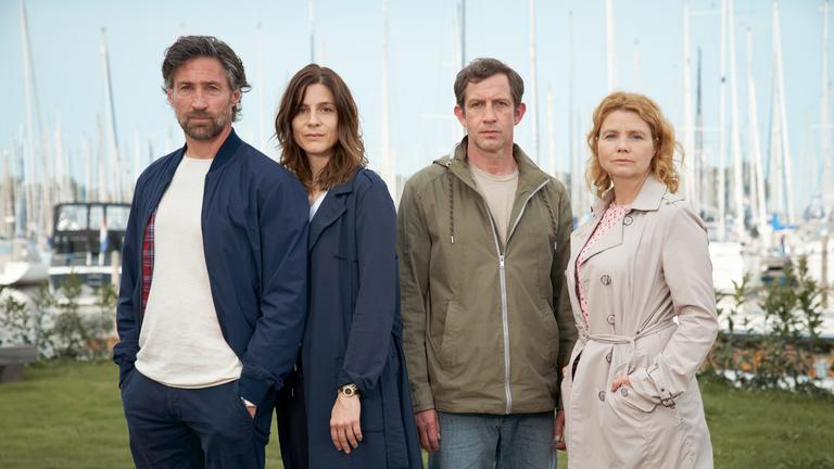 "Leben über Kreuz": Sebastian Blumberg (Benjamin Sadler), Caren Blumberg (Christina Hecke), Jan Kempe (André Szymanski) und Birthe Kempe (Annette Frierm) stehen dicht beieinander und im Hintergrund erkennt man mehrere Segelboote.