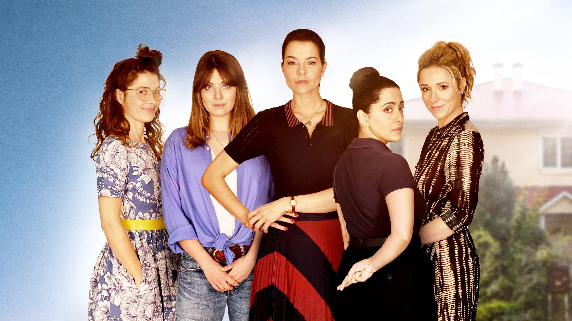 "Wendehammer - Stille Wasser": Meike (Meike Droste), Julia (Alice Dwyer), Franziska (Susan Hoecke), Samira (Elmira Rafizadeh) und Nadine (Friederike Linke) stehen in einer Reihe nebeneinander und lächeln in die Kamera. Im Hintergrund ist verschwommen ein Wohnhaus zu erkennen.