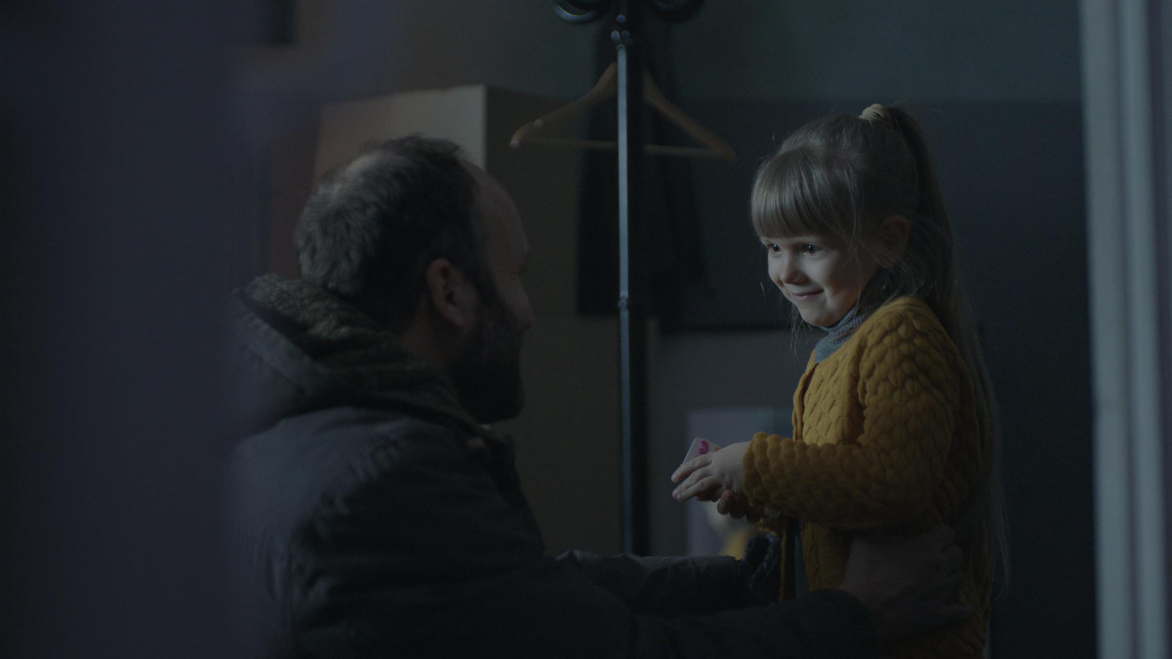 "Hide & Seek - Gefährliches Versteckspiel: Neue Partner": Jevgenij Borovko (Oleksandr Kobzar) steht in einer Wohnung seiner siebenjährigen Tochter Alina (Azalia Tkachuk) gegenüber, die auf einer Kommode sitzt. Sie schauen sich lächelnd und liebevoll an.