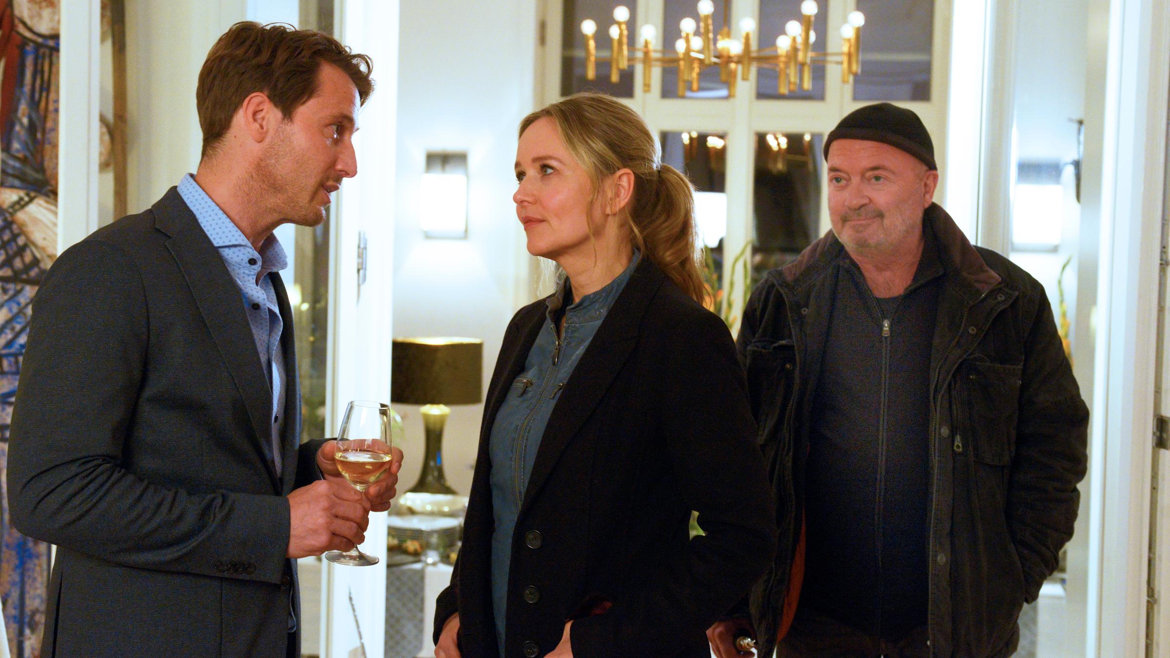 "Ein starkes Team - Schulzeit": Linett Wachow (Stefanie Stappenbeck) und Otto Garber (Florian Martens)stehen Hendrik Hübner (David Rott) in einem großen Wohnzimmer gegenüber. Es ist Nacht und Hendrik hält ein Weinglas in den Händen.