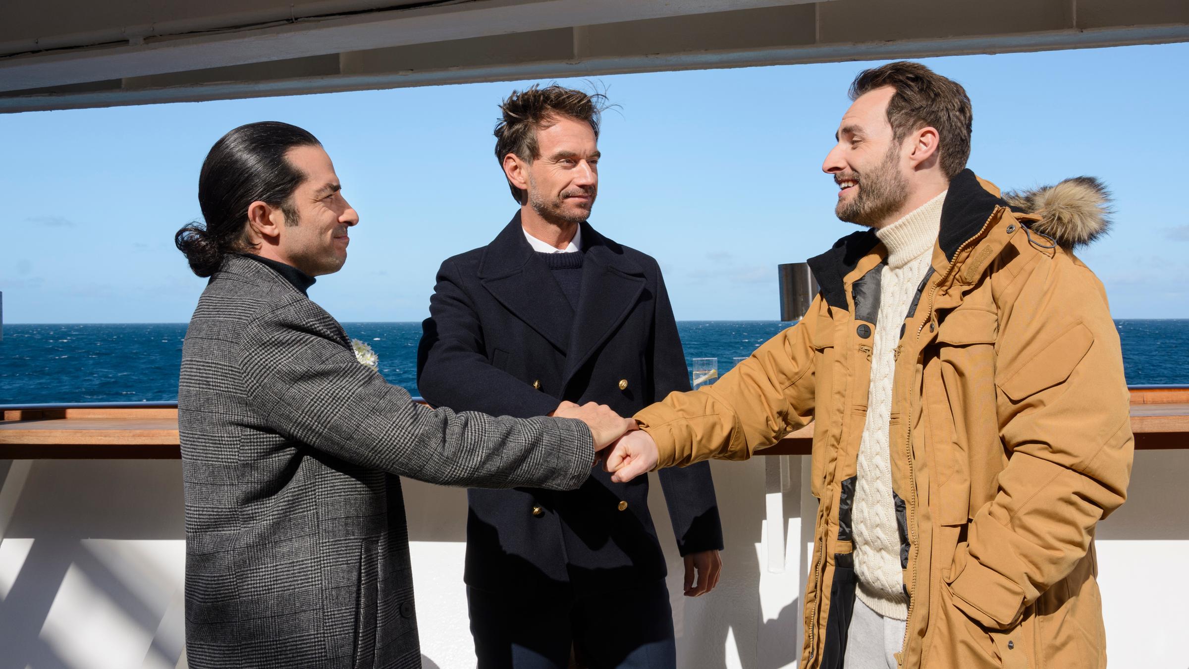 "Das Traumschiff -  Lappland": An Deck des Schiffs stehen Max Parger (Florian Silbereisen), Patrick Steiner (Daniel Fritz) und Maik Berghammer (Tayfun Baydar) zusammen. Die Freunde legen die Hände übereinander und lächeln sich an.