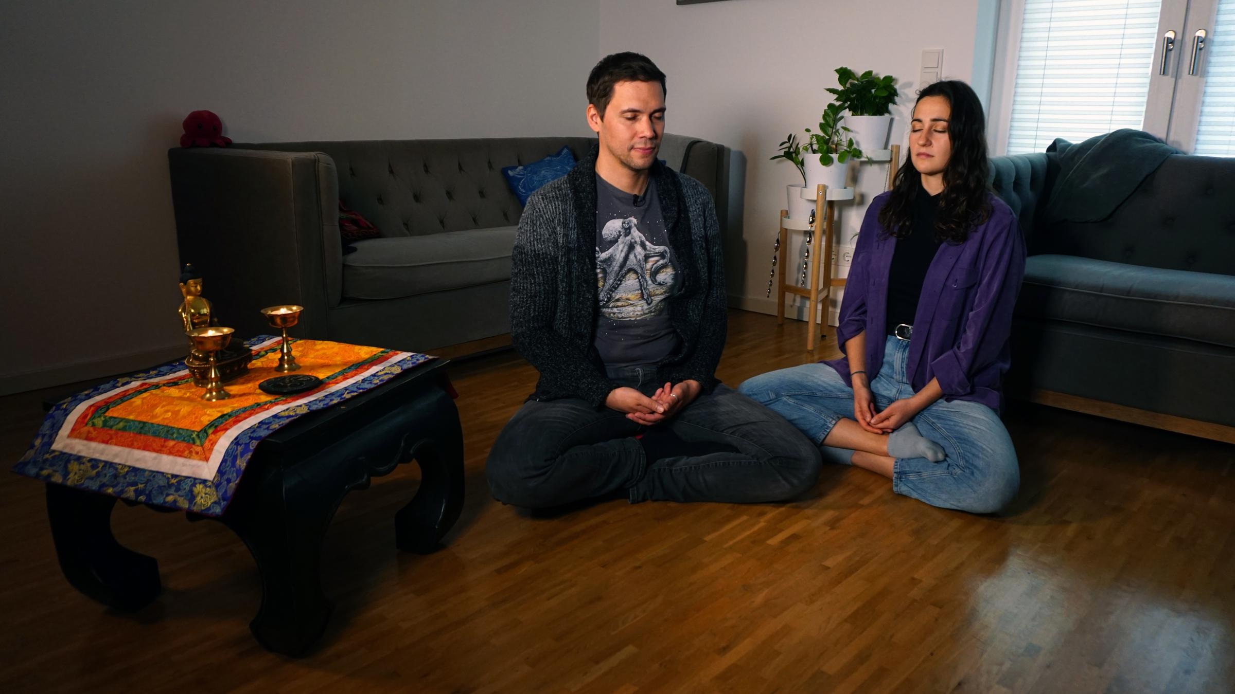 "37°Leben - Warum glaubst du? Die Hoffnung": Benjamin (l.) und Saadet (r.) sitzen im Lotussitz auf einem Boden in einem Wohnzimmer und meditieren mit geschlossenen Augen. Auf einem kleinen Tischchen neben ihnen stehen eine kleine, goldene Buddhastatue und zwei goldene Kelche.