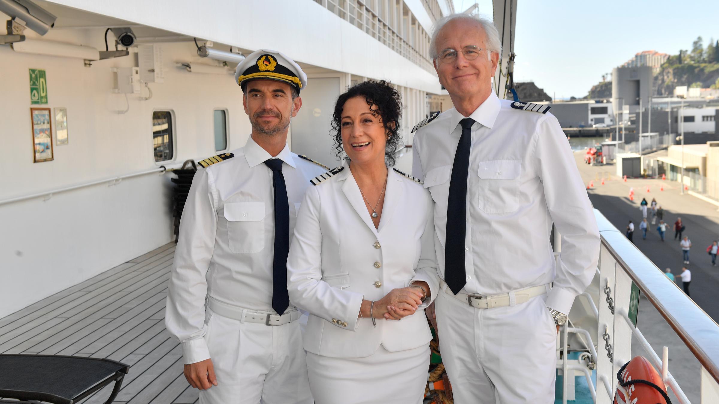 "Das Traumschiff - Walvis Bay": An Deck des Schiffs, dass im Hafen ankert, steht Hanna Liebhold (Barbara Wussow) lachend zwischen Kapitän Max Parger (Florian Silbereisen) und Oskar Schifferle (Harald Schmidt).