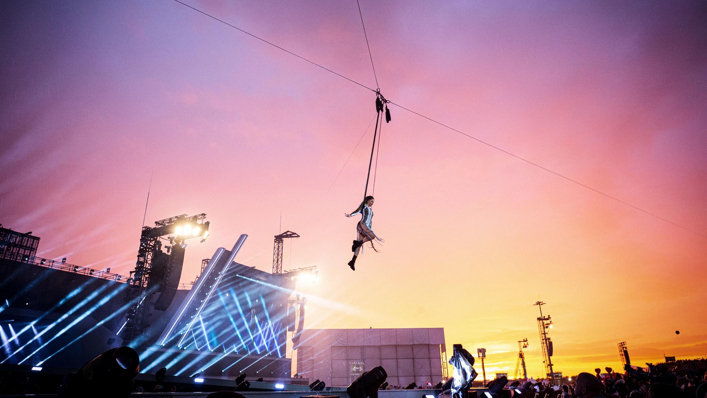 "Helene Fischer - Wenn alles durchdreht": Helene Fischer hängt in einer Flugkonstruktion und fliegt über das Publikum. Sie hat ihre Arme ausgestreckt. Im Hintergrund ist die Bühne und ein buntes Himmelbild zu sehen.