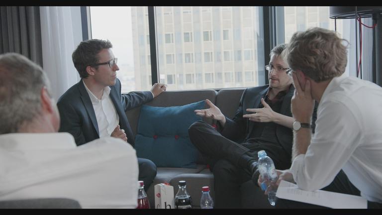 "Hinter den Schlagzeilen": Auf einem Sofa sitzen Journalist Bastian Obermayer und Edward Snowden. Vor ihnen sitzen die Journalisten Georg Mascolo und Frederik Obermaier.