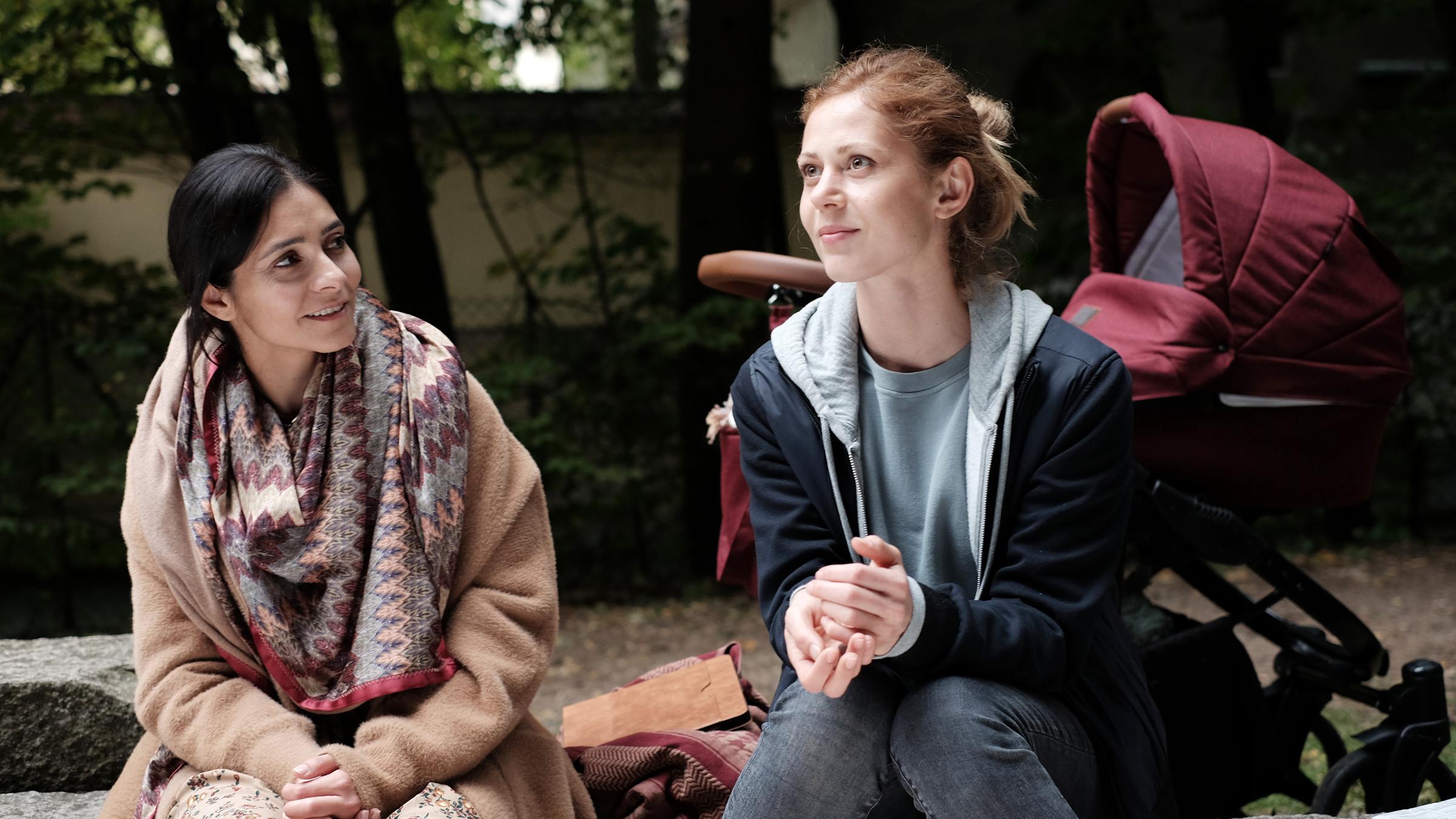 "In falschen Händen": Zwei junge Frauen, Nika (Pegah Ferydoni) und Manu (Katharina Schlothauer), unterhalten sich angeregt auf einem Spielplatz. Hinter ihnen steht ein Kinderwagen.