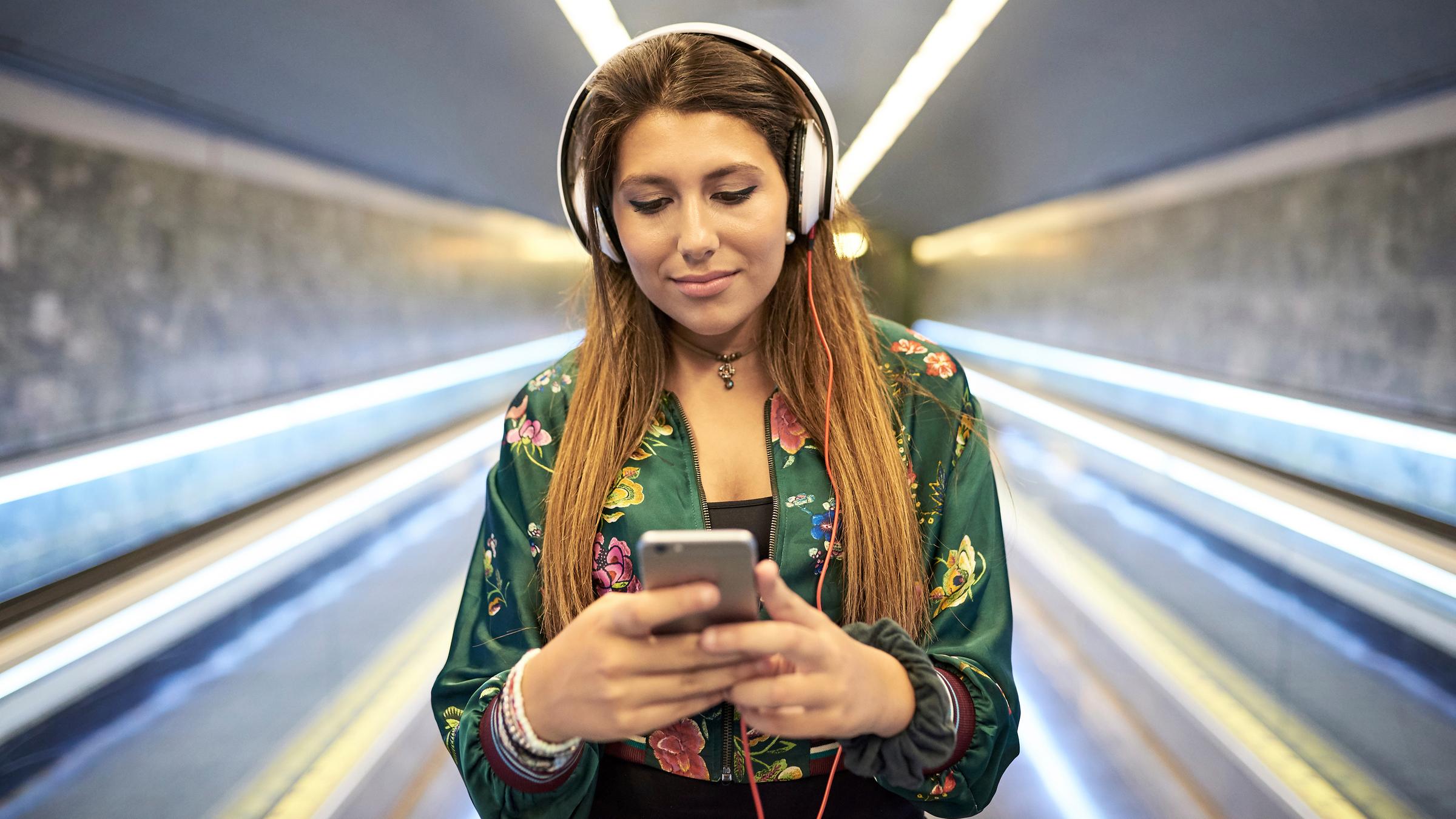 "This is Spotify - Songs und Stars auf Abruf": Eine junge Frau mit Kopfhörern streamt Musik über ihr Smartphone.