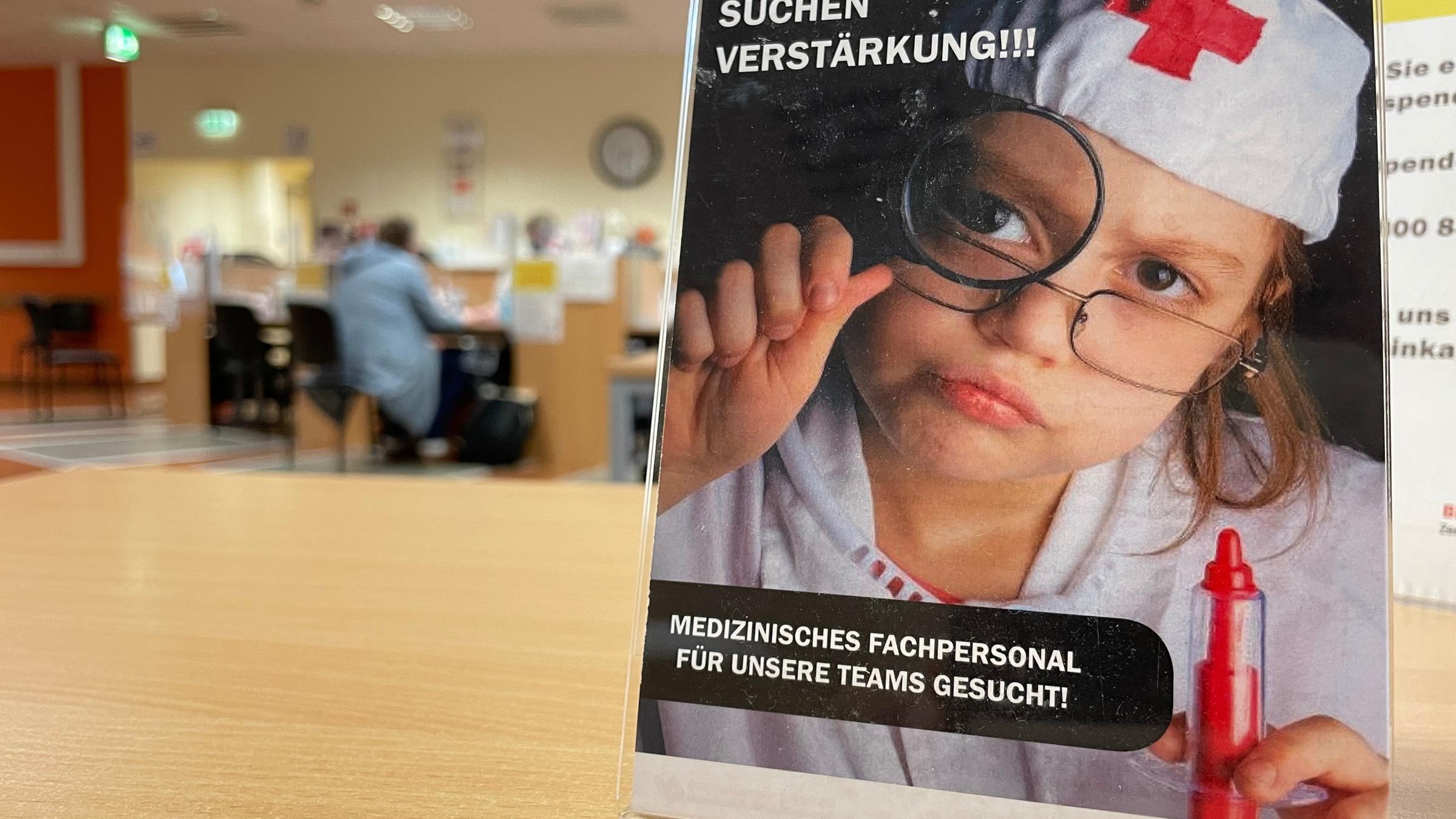 "ZDF.reportage: Personal dringend gesucht - Wer macht die Arbeit?": Auf einem Plakat mit der Überschrift "WIR SUCHEN VERSTÄRKUNG!!!" ist ein Kind zu sehen, das suchend durch eine Lupe blickt. Das Kind ist als medizinische Fachkraft verkleidet.