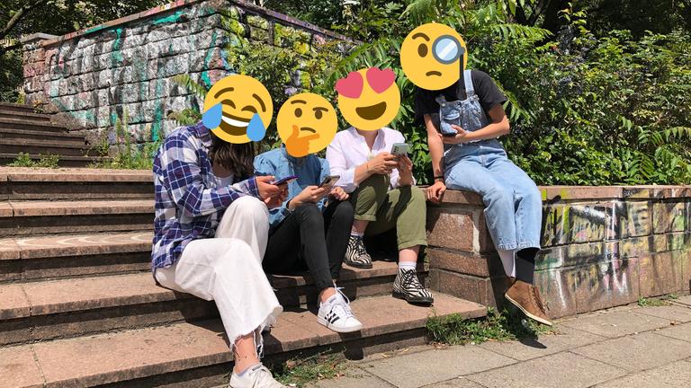 "Die Emojikalypse": Vier Jugendliche sitzen draußen auf einer Treppe, anstatt Köpfen sind Emojis auf ihre Schultern montiert.