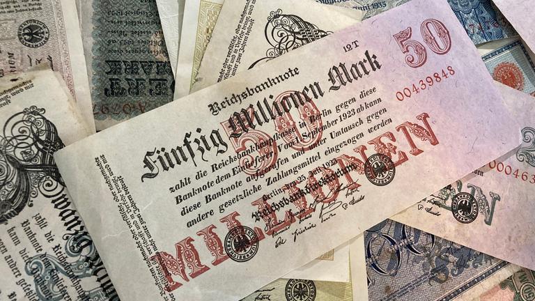 "Inflation – Die Angst vor dem Wohlstandskiller": Ansicht mehrerer Geldscheine. In der Mitte des Bildes ist ein großer Geldschein zu sehen, auf dem die Aufschrift "Fünfzig Millionen Mark" steht.