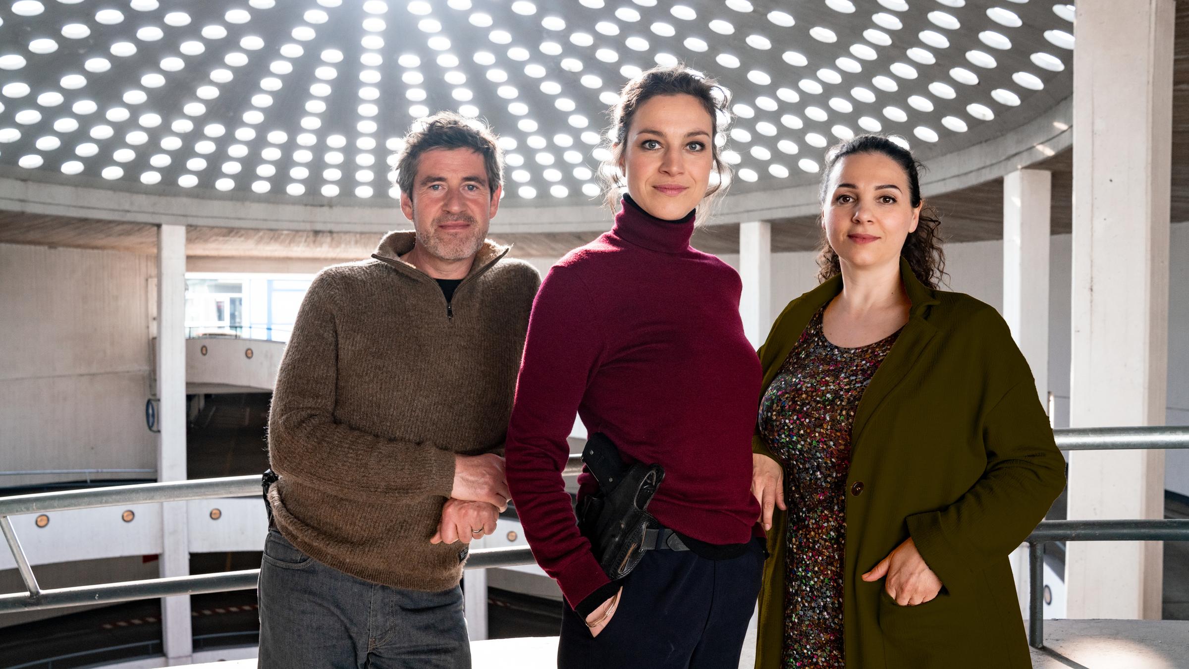 "Was wir verbergen": Georg König (Stephan Szász), Katharina Tempel (Franziska Hartmann) und Dela Tahiri (Hanife Sylejmani) stehen nebeneinander im Parkhaus und blicken lächelnd in die Kamera.