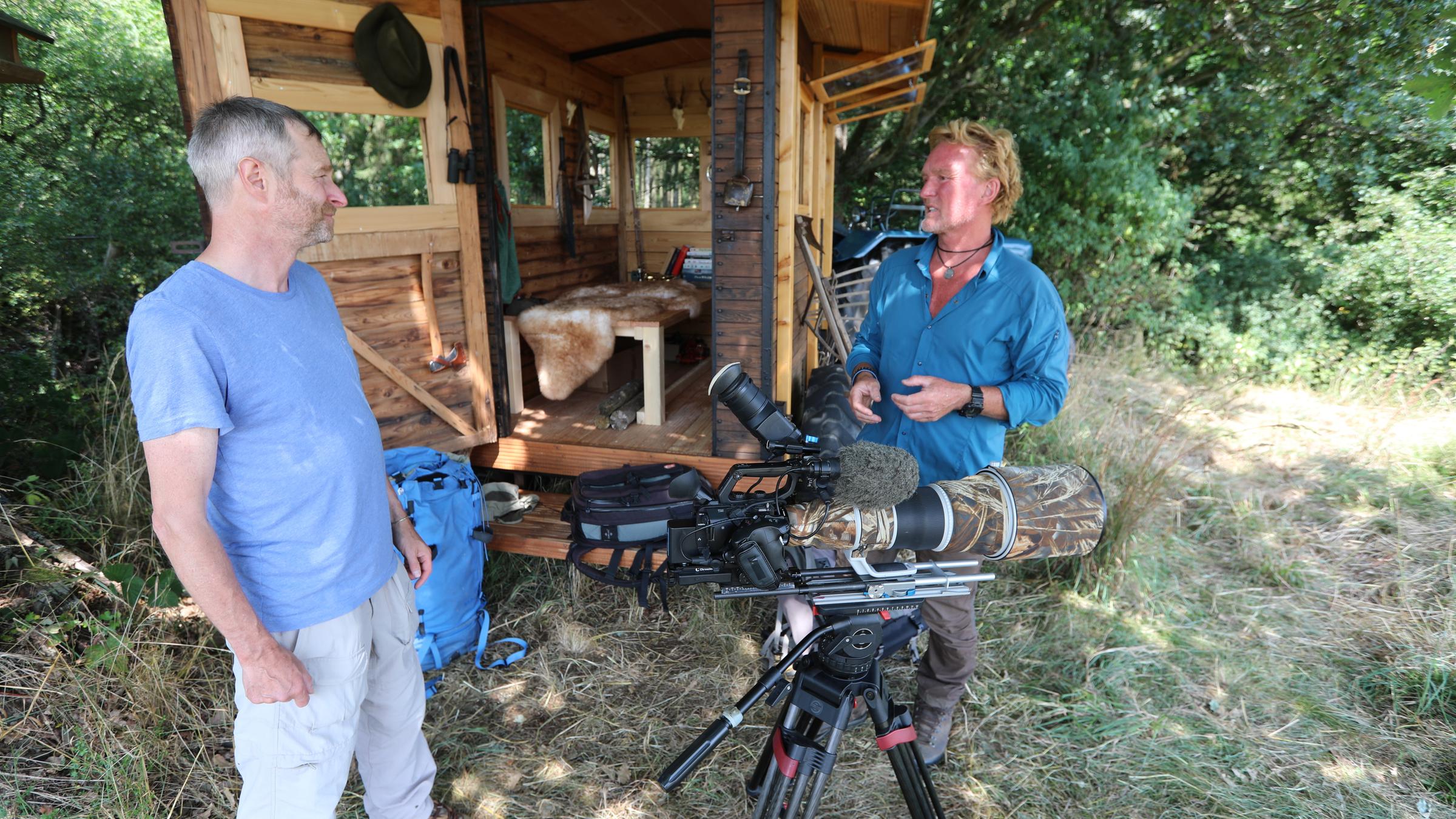 "Terra X: Kielings wilde Welt - Der Bärenmann": Andreas Kieling und Frank Gutsche vor dem für die Dreharbeiten in der Eifel umgebauten Wagen. Im Hintergrund Bäume. Vorne sieht man eine Kamera.