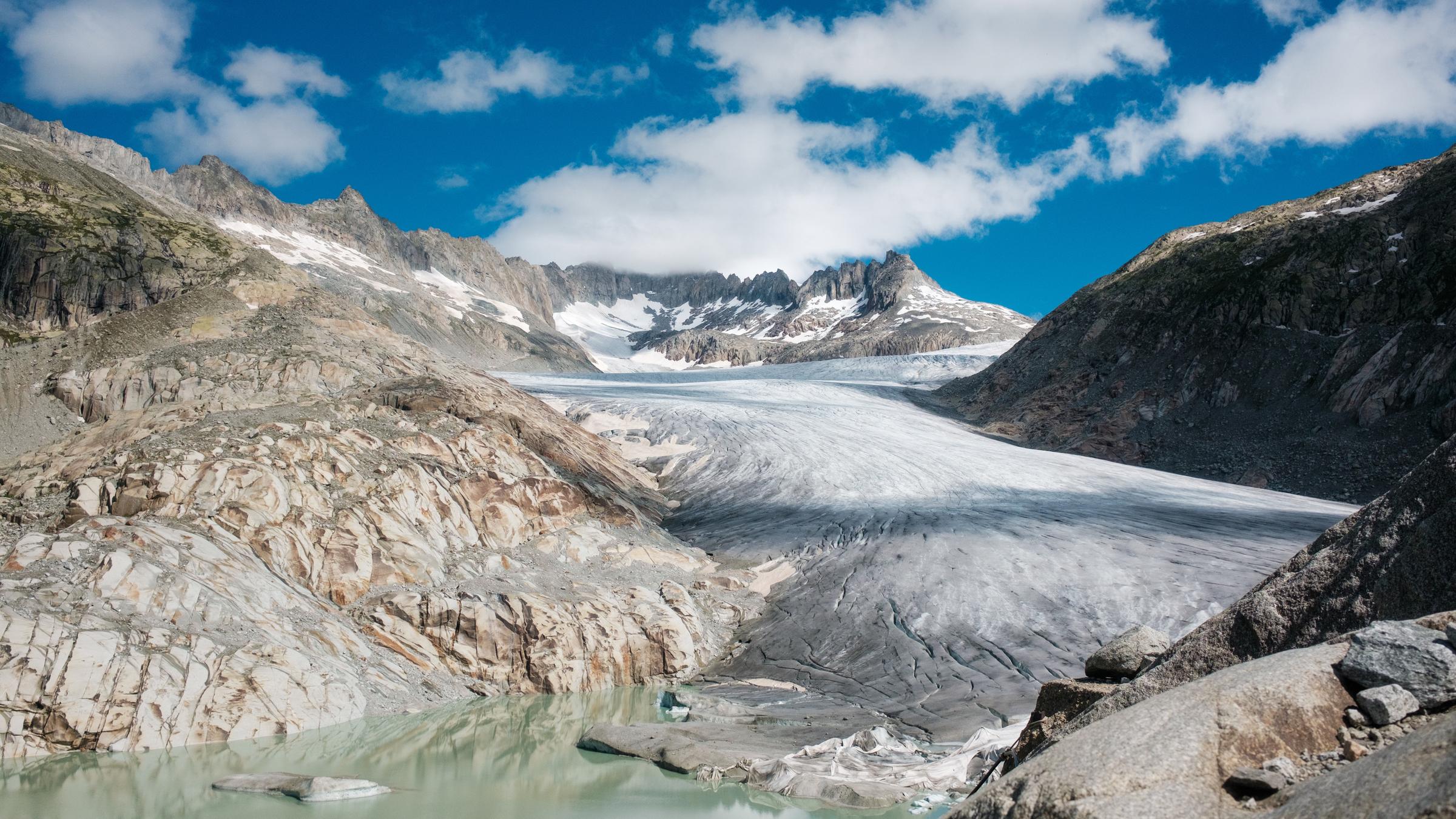 "ZDFzeit: Alpen in Gefahr - Klimakrise in den Bergen": Vor einem blauen Himmel liegt ein Bergpanorama mit einer Gletscherzunge, die in einem Tümpel endet.