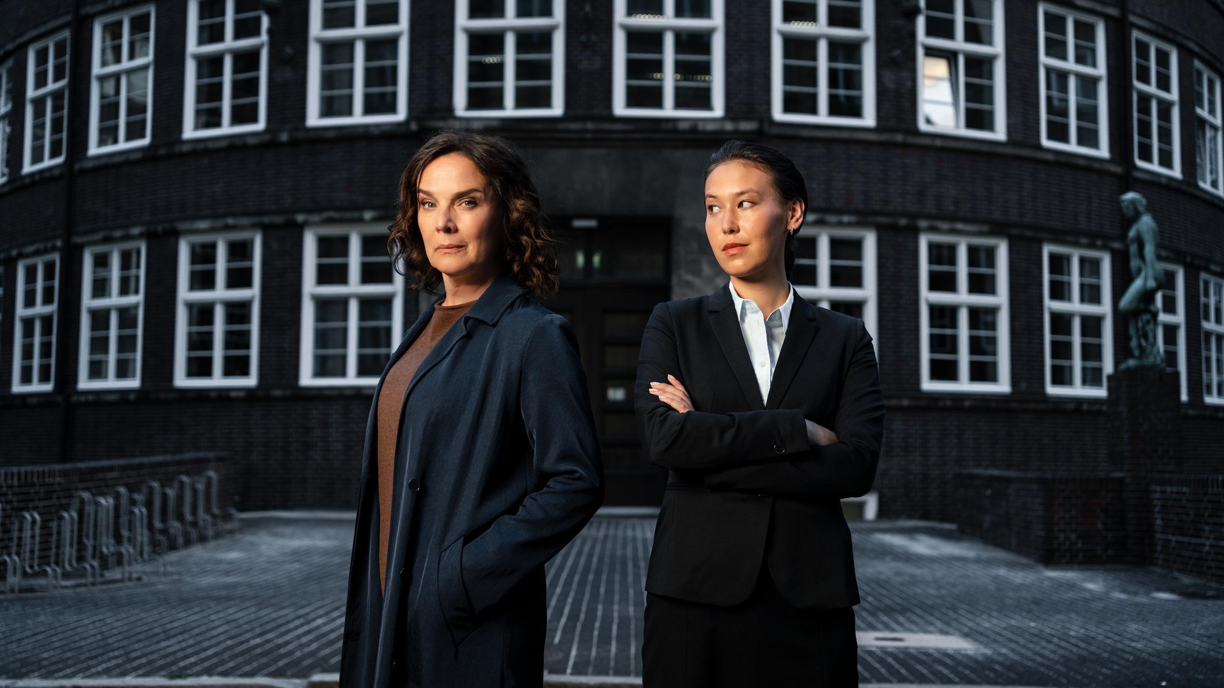 "Conti - Meine zwei Gesichter": Doppelporträt von Désirée Nosbusch und Malaya Stern Takeda in ihrer jeweiligen Rolle als Rechtsanwältin Anna Conti und Staatsanwältin Henry Mahn. Die beiden Schauspielerinnen stehen Schulter an Schulter vor einem Backsteingebäude mit weißen Fenstern.
